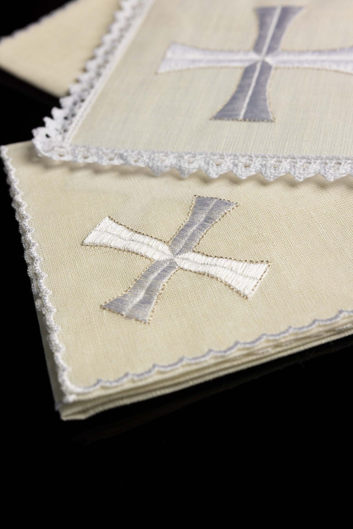 Folded view of chalice linens with delicate cross embroidery, cream linen with a white and silver cross