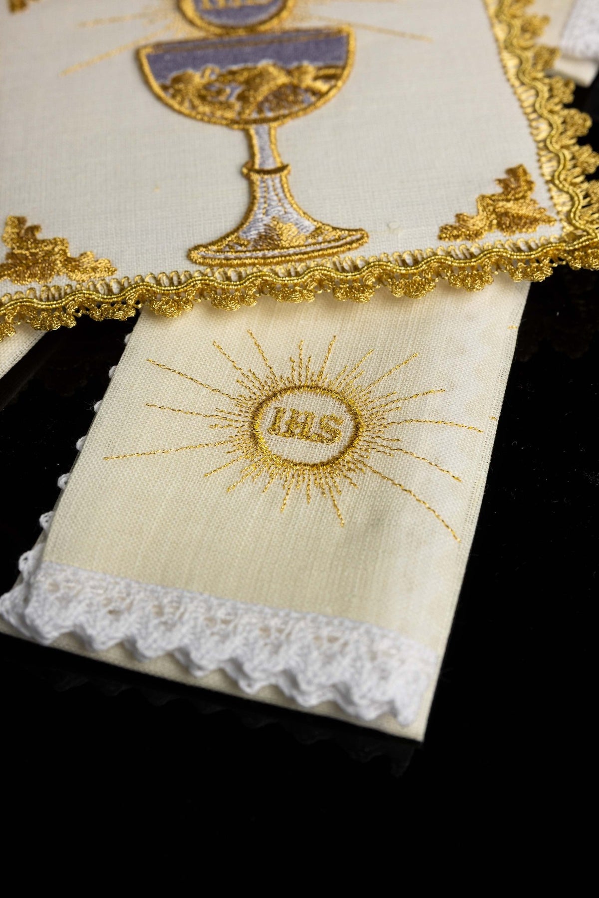 Close-up of the chalice set showing an IHS sunburst on an ivory linen with white lace