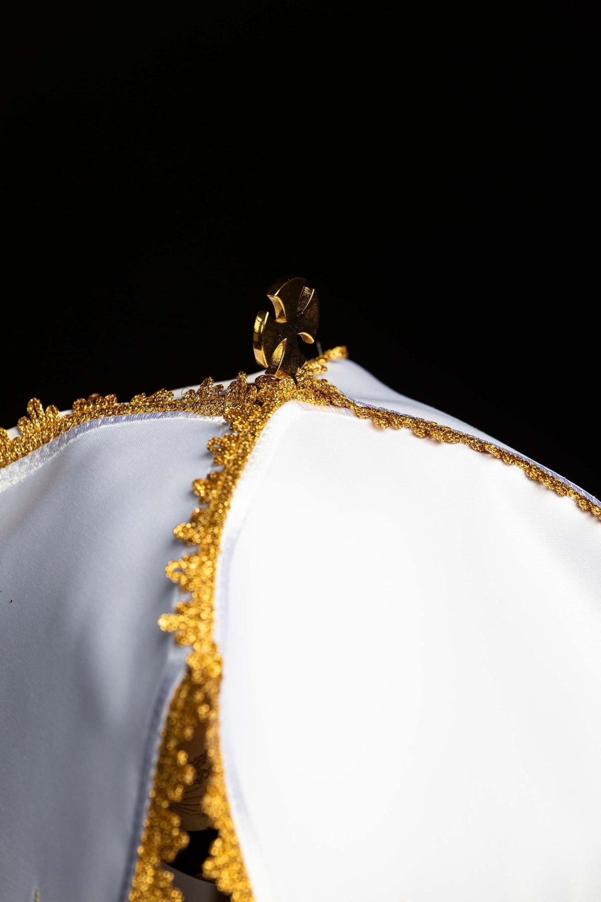 Top detail of the ciborium veil showing its gold cross-shaped clasp and decorative trim