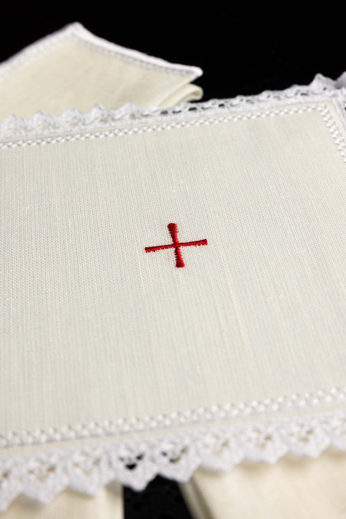 Close-up of the altar linen showing a small red embroidered cross and white lace edge