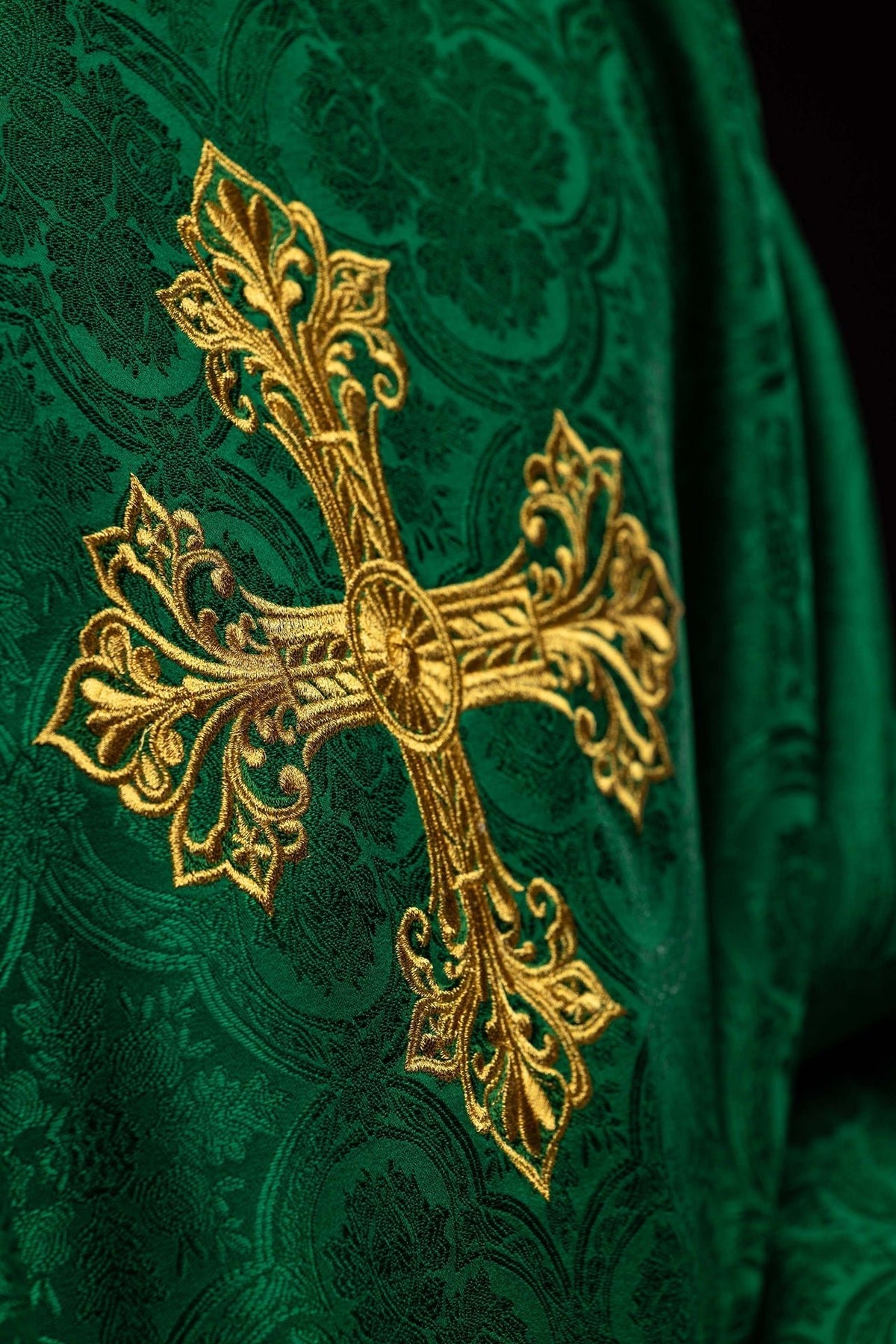 Close-up of the gold embroidered cross on a green chasuble with jacquard fabric
