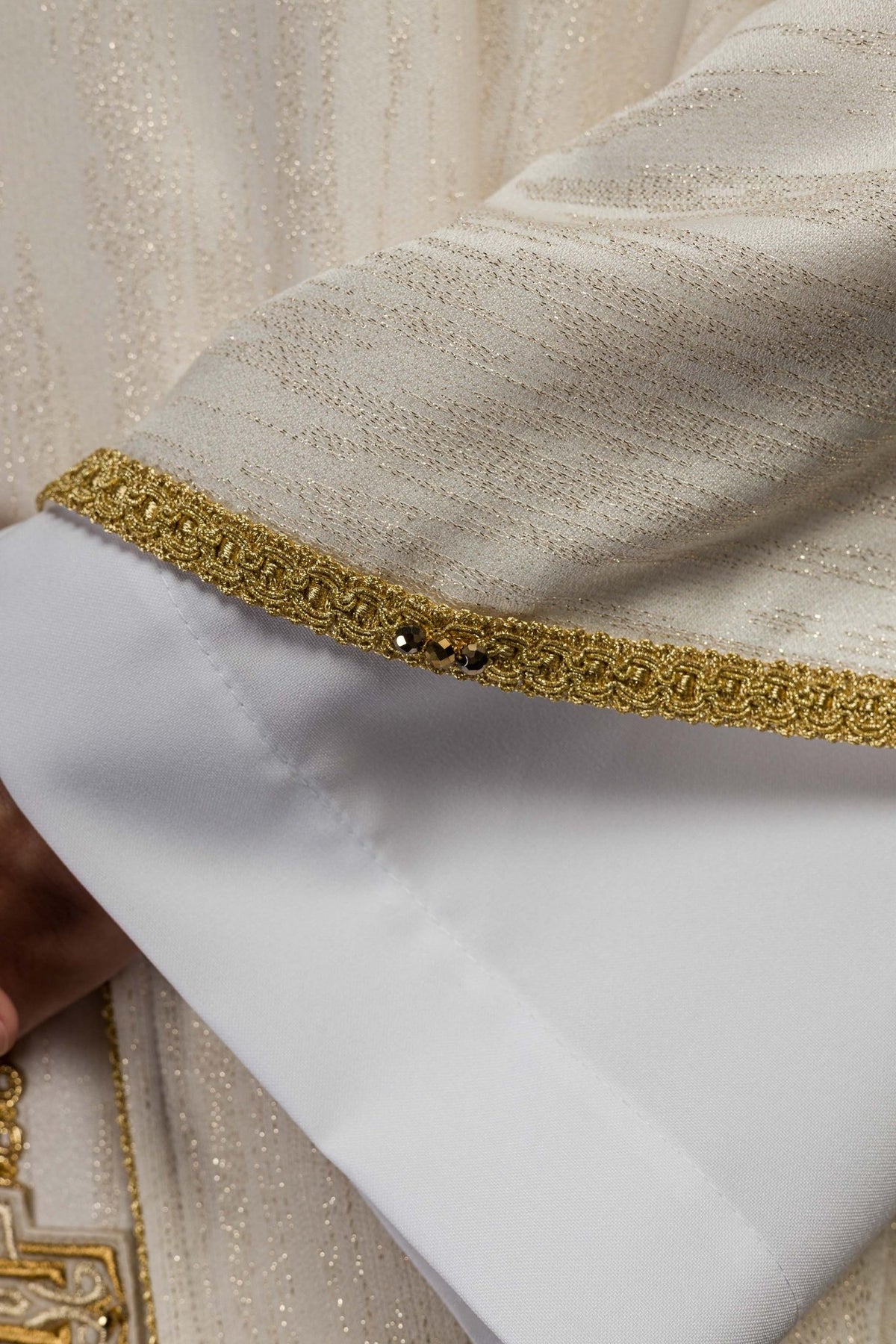 Close-up of ecru chasuble's shimmering fabric and gold sleeve trim