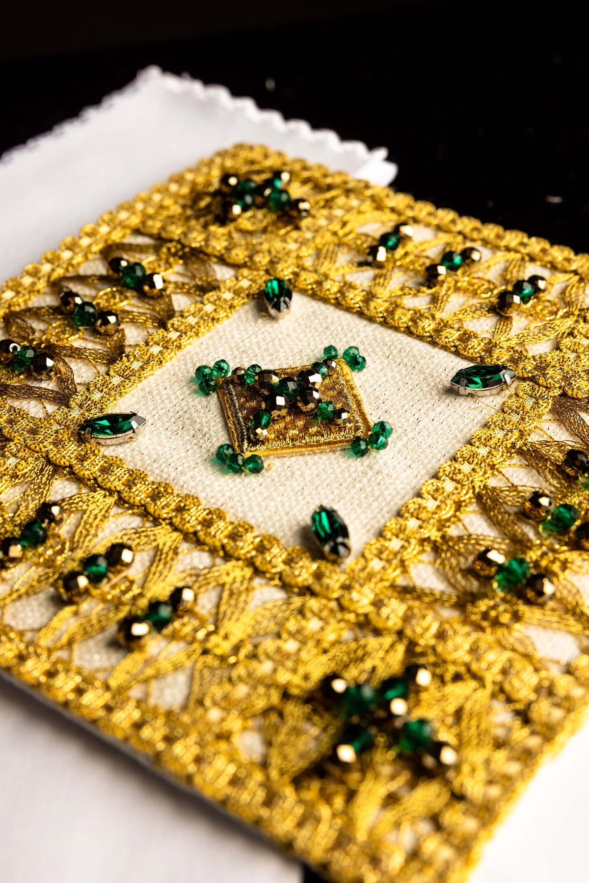 Close-up of the altar linen set's chalice pall showing gold trim, green stones, and central square motif