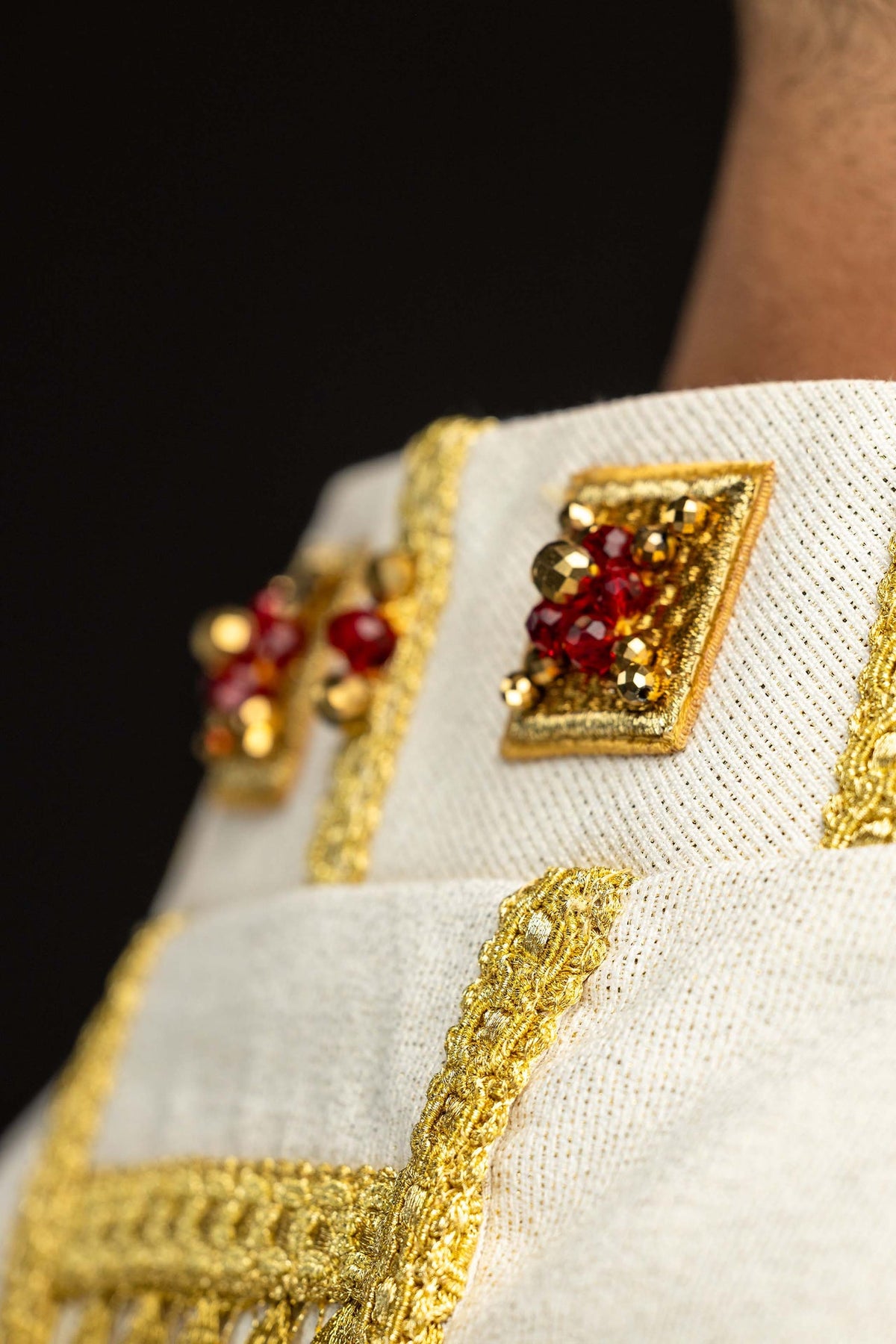 Detail of the white handmade chasuble with a square gold motif and red natural stones