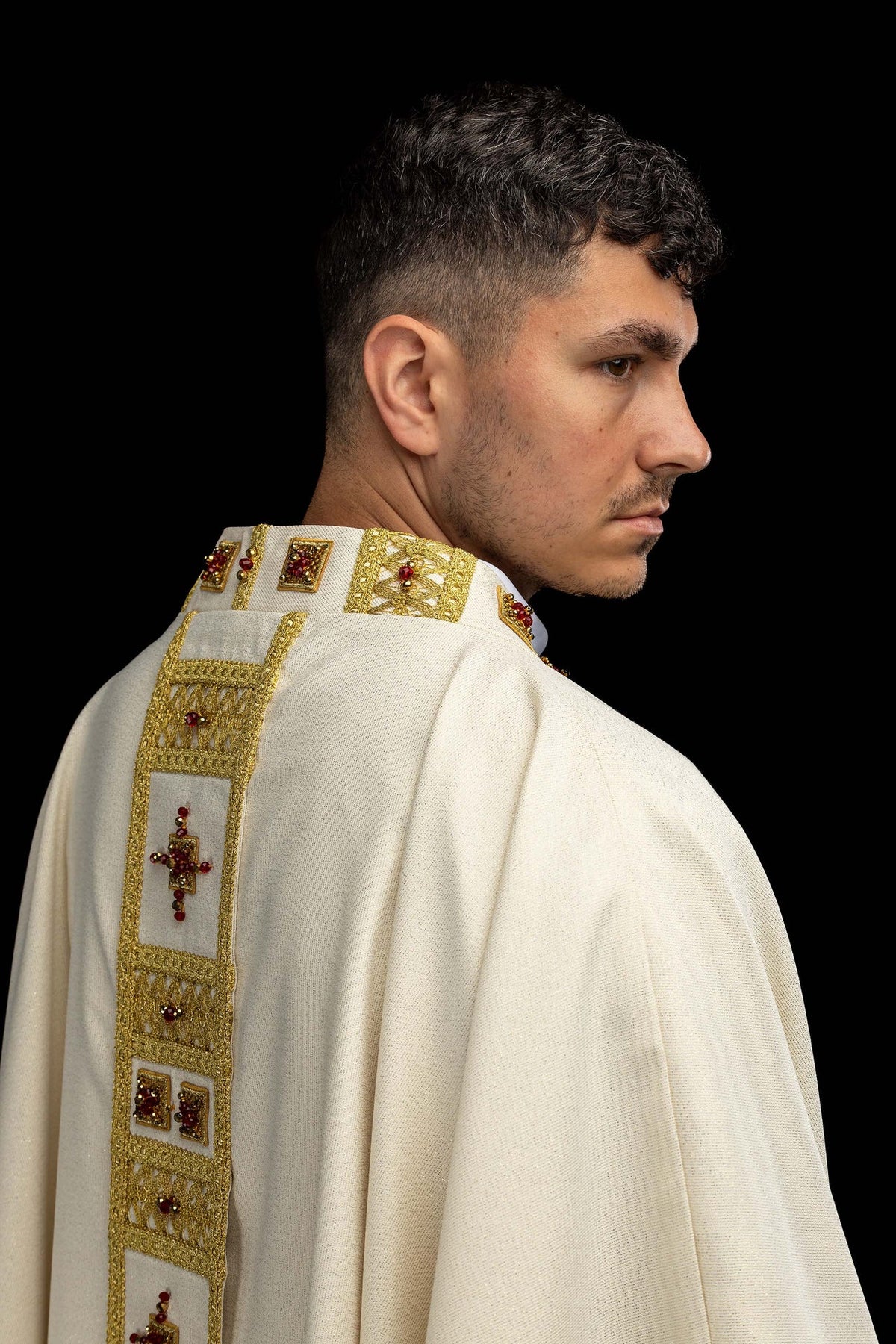 Side detail of the white handmade chasuble with gold openwork trim and red stones