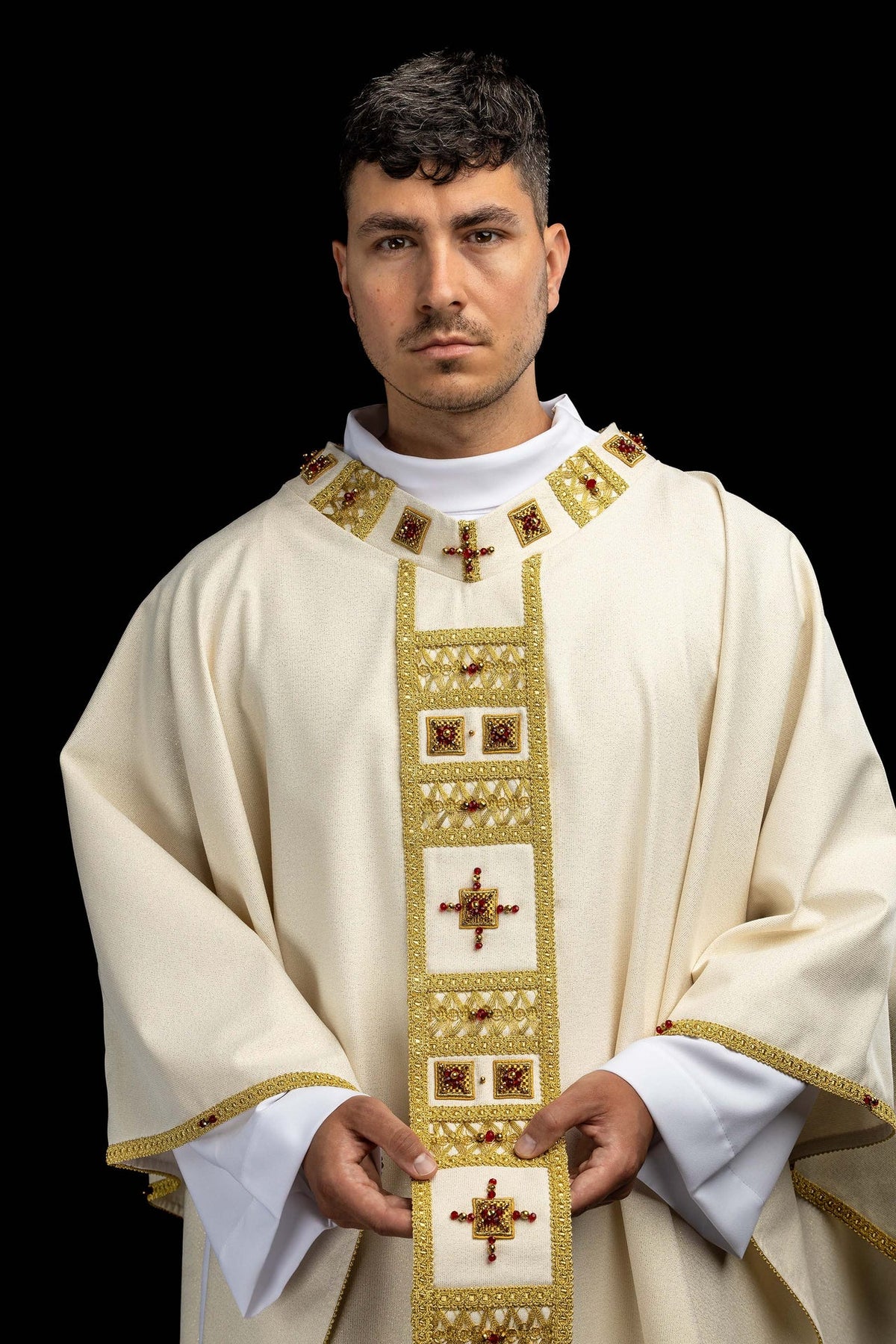 Worn front view of a white handmade chasuble with gold trim, crosses, and red natural stones