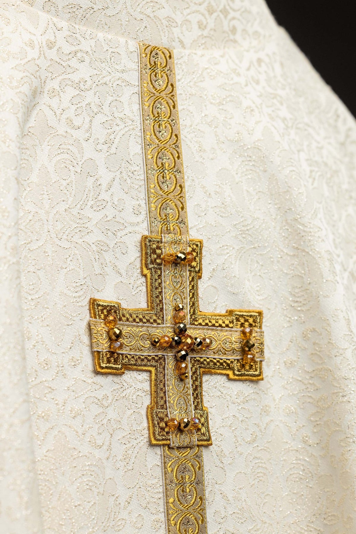 Close-up of a raised gold cross with amber stones on the chasuble