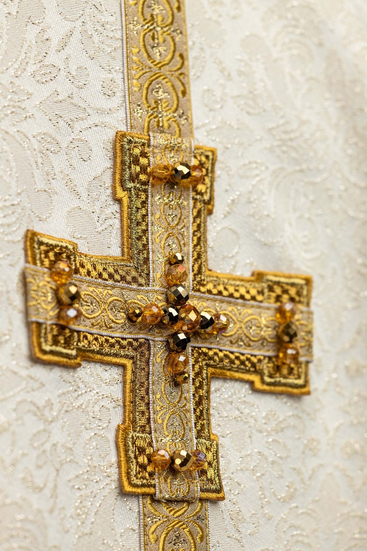 Close-up of a handmade chasuble with embroidered 3D crosses and natural stones in gold and ivory
