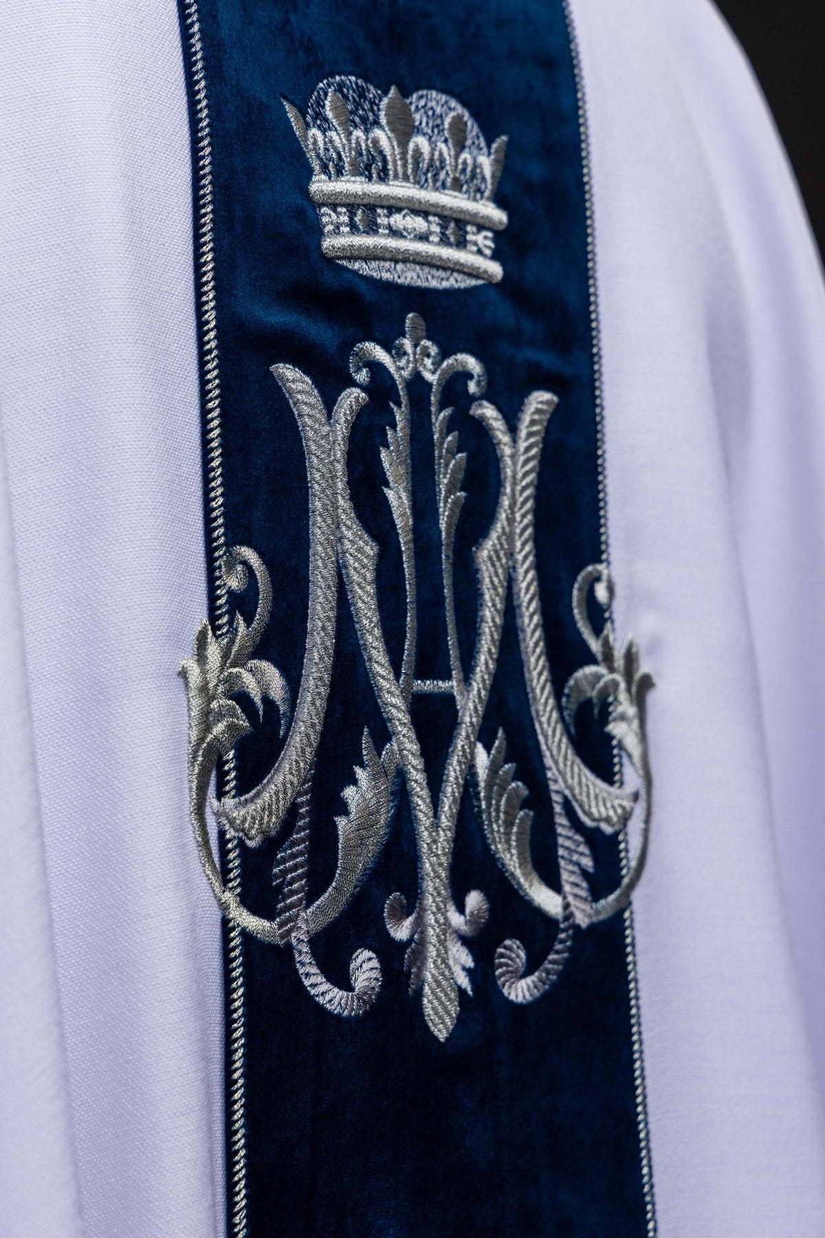 Close-up of the chasuble back showing crowned silver Marian monogram on blue velvet