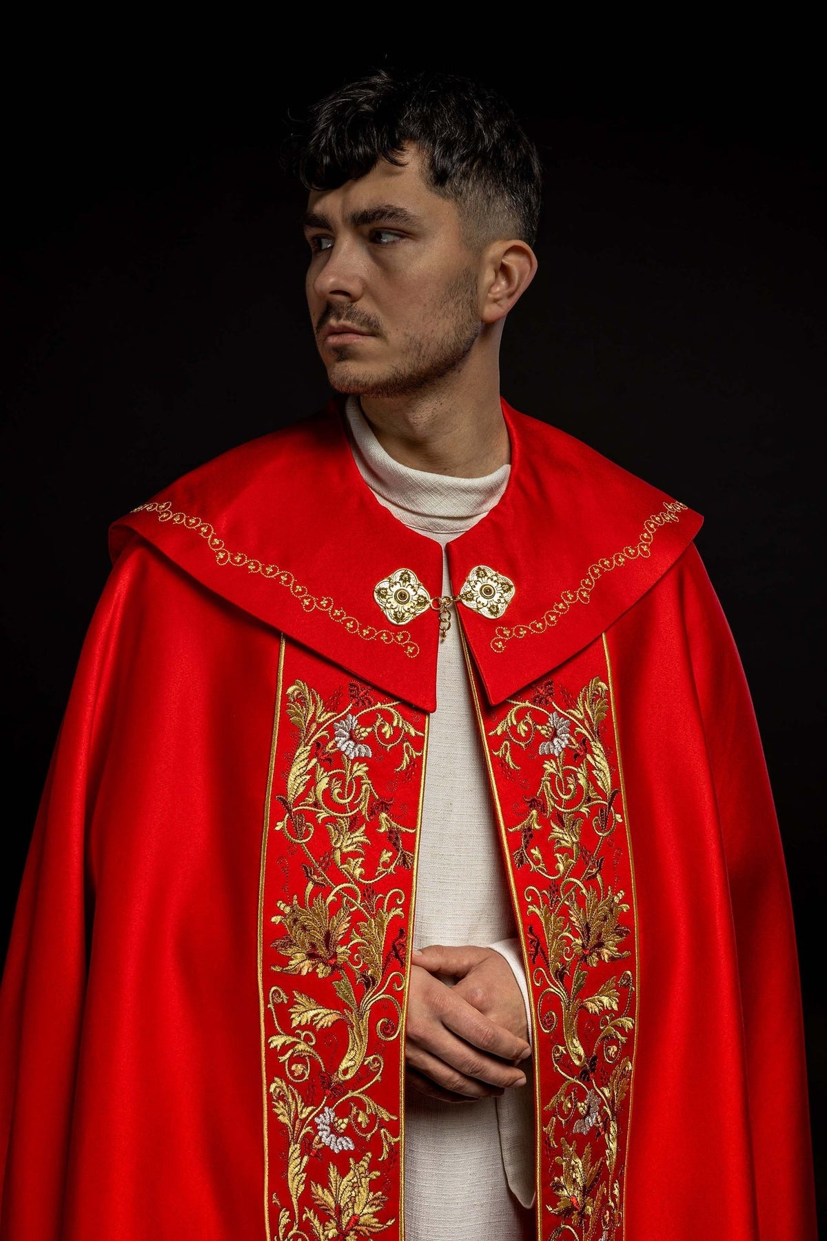 Back view of red liturgical cope with gold IHS embroidery, floral border and hanging tassel