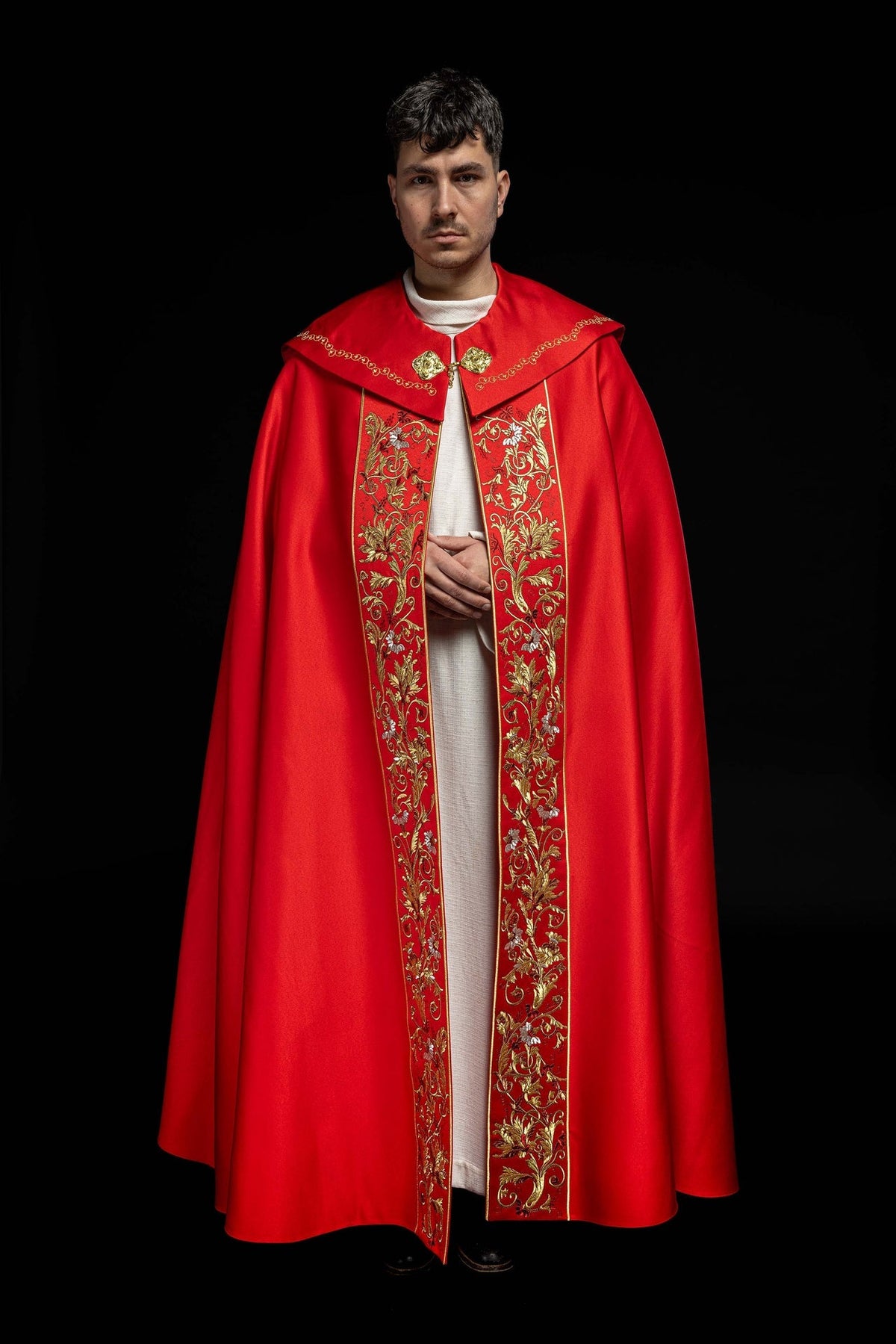 Front view of red liturgical cope with gold floral embroidered panels and decorative clasps