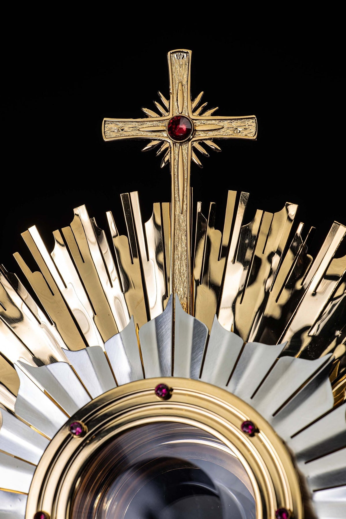Upper detail of gilded brass monstrance with textured cross and central ruby