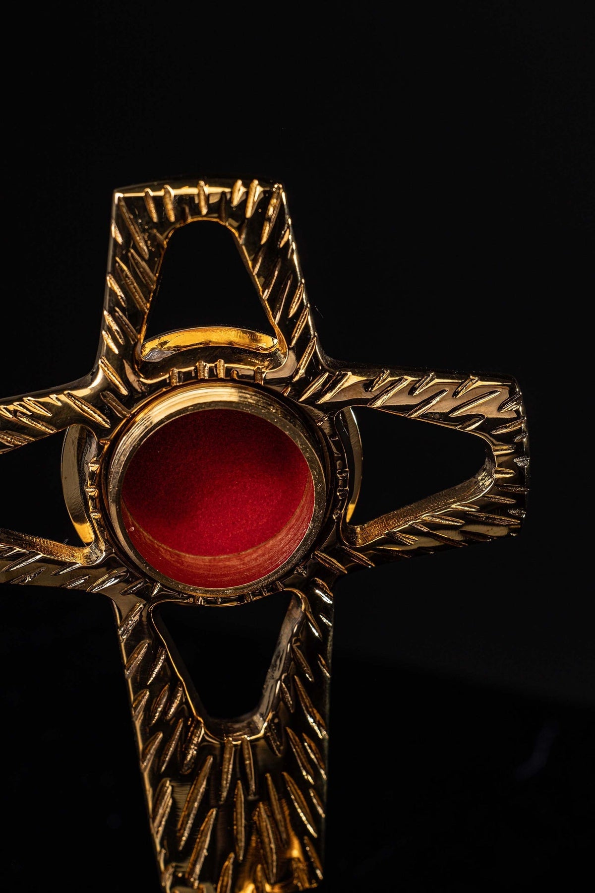 Close-up of cross-shaped brass reliquary with red center and engraved rays