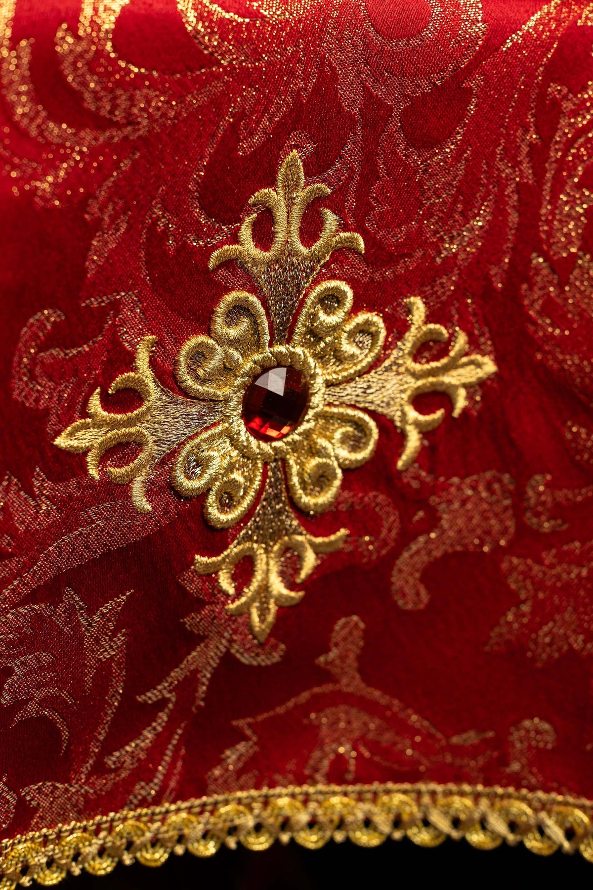 Close-up of a red chalice veil with embroidered gold cross and red stone