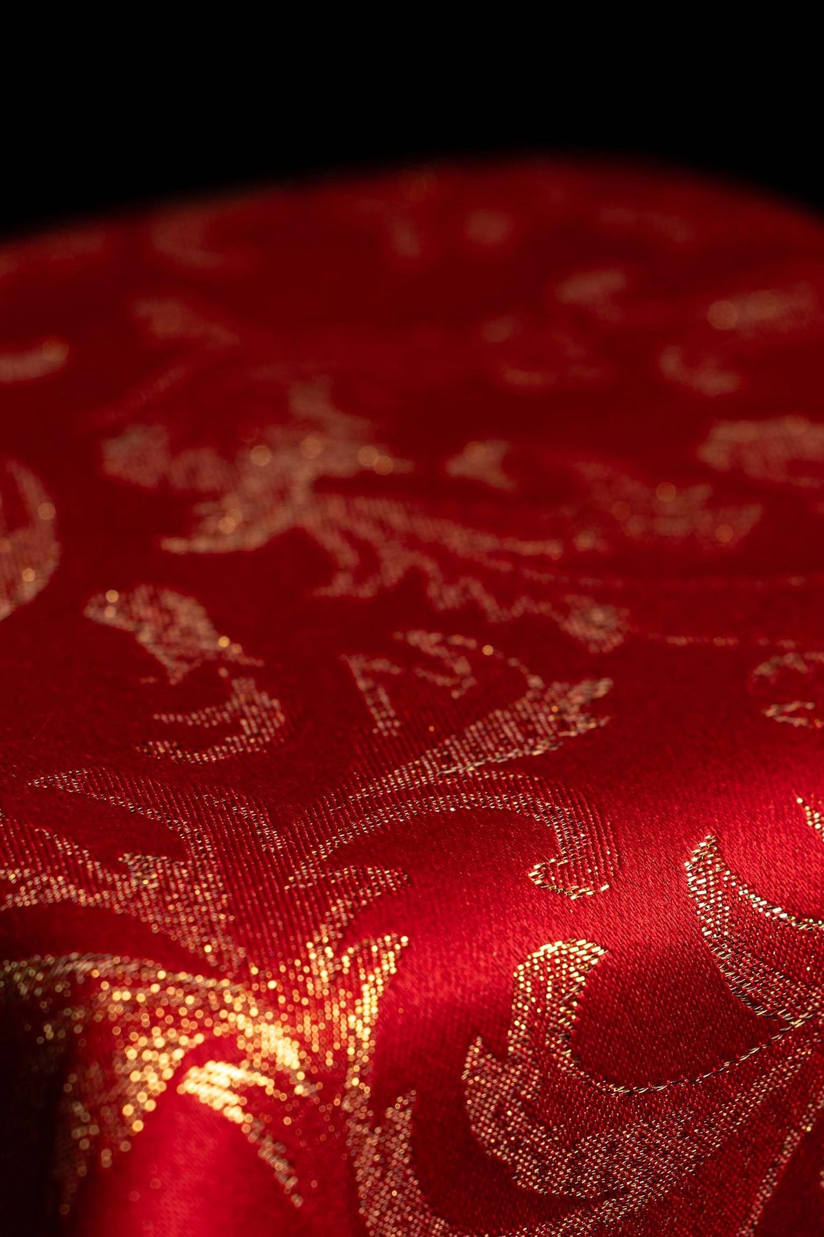 Fabric detail of a red chalice veil with gold brocade pattern