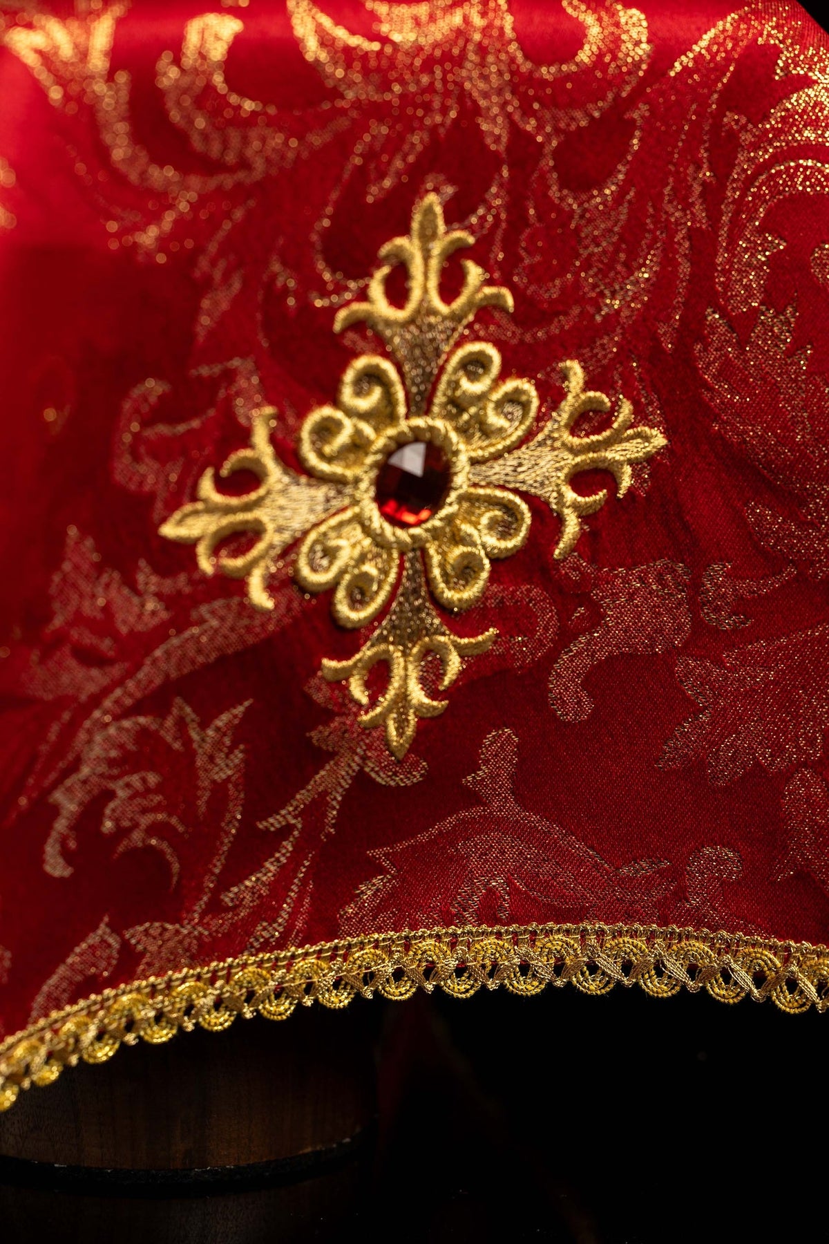 Close-up of a red chalice veil with embroidered gold cross, red stone, and gold trim