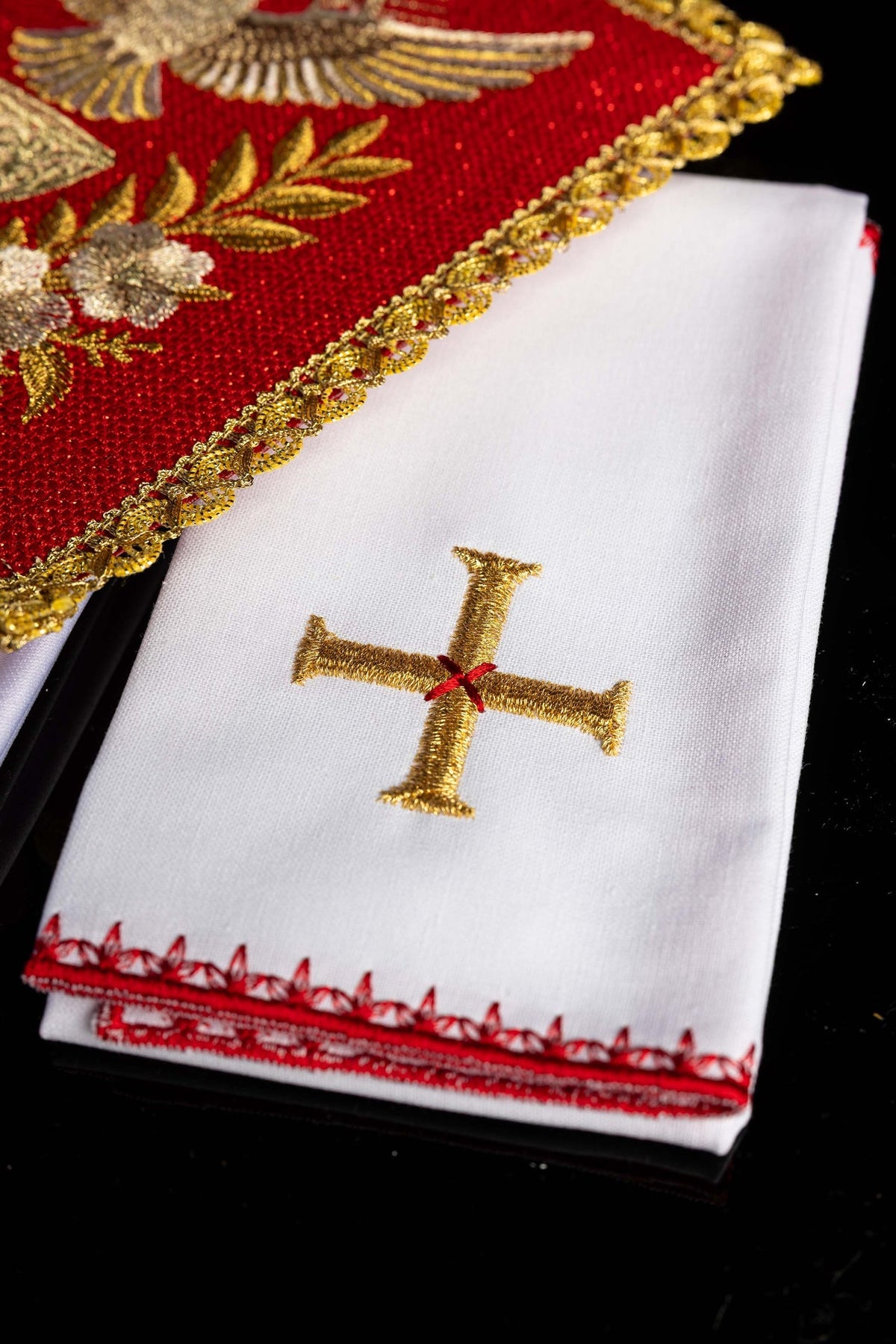 Folded altar linen set detail showing a gold embroidered cross and red decorative border