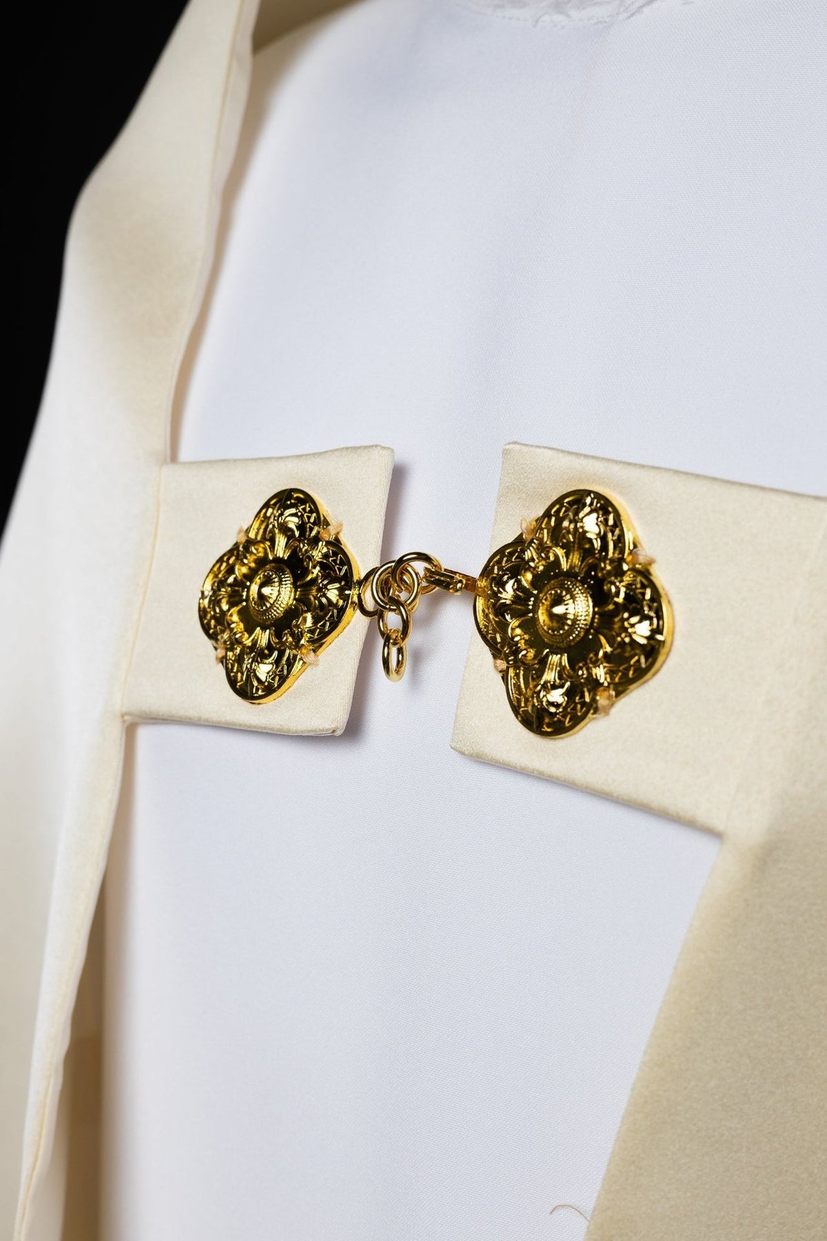Close-up of ecru humeral veil clasp with ornate gold floral medallions