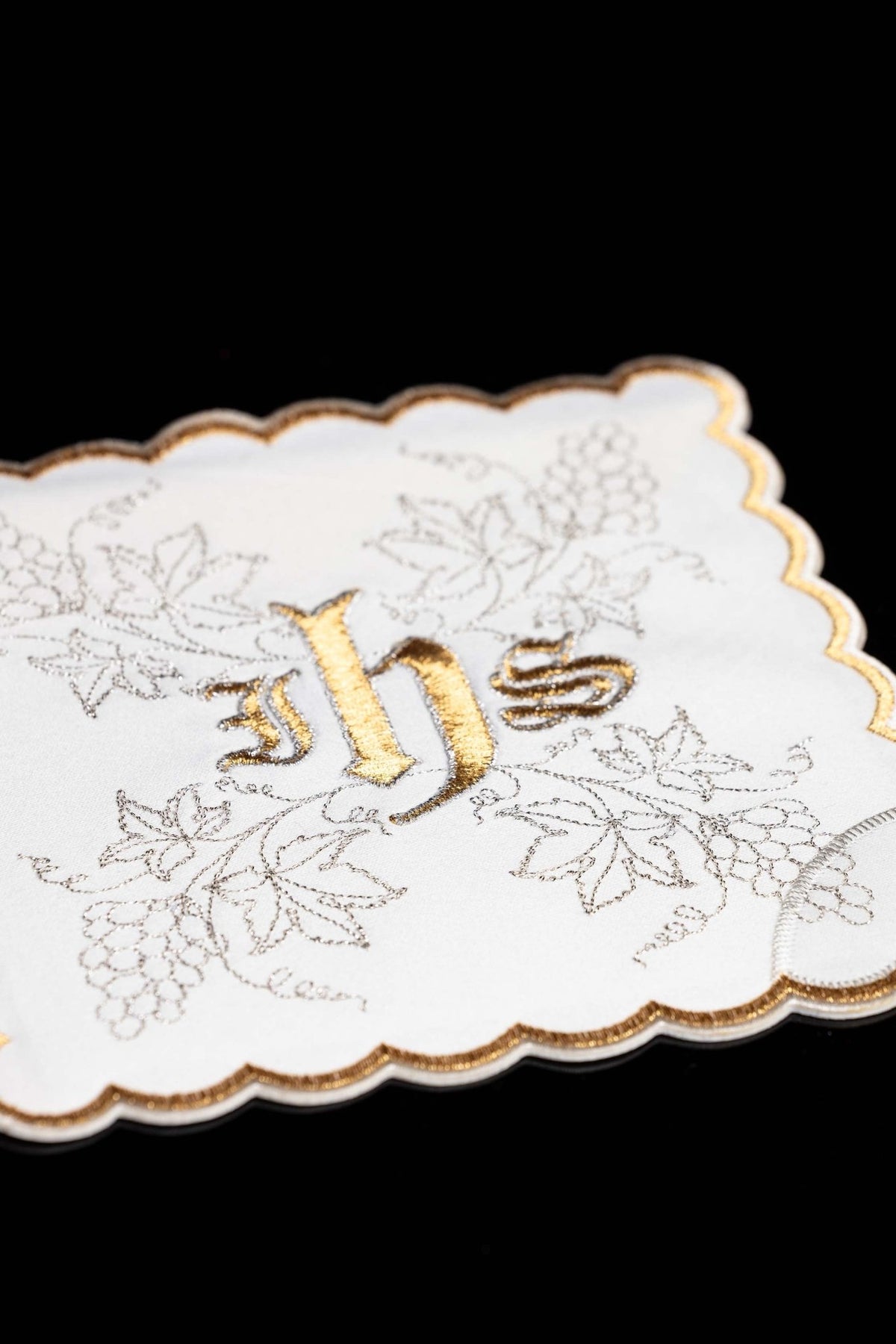 Close-up of a white chalice pall with gold IHS and silver grapevine embroidery