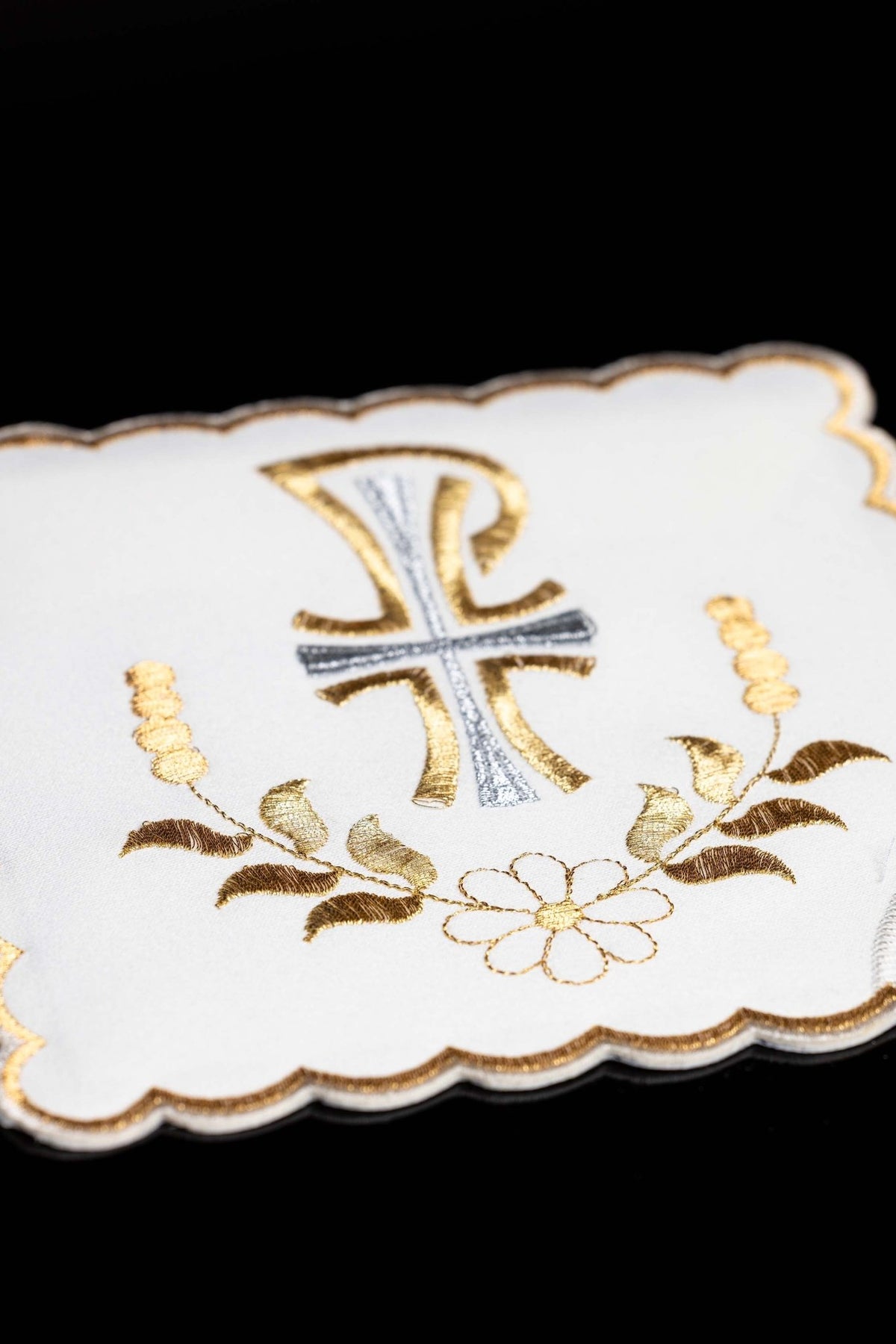 Close-up of a white chalice pall with PAX embroidery, gold botanical motif, and scalloped trim