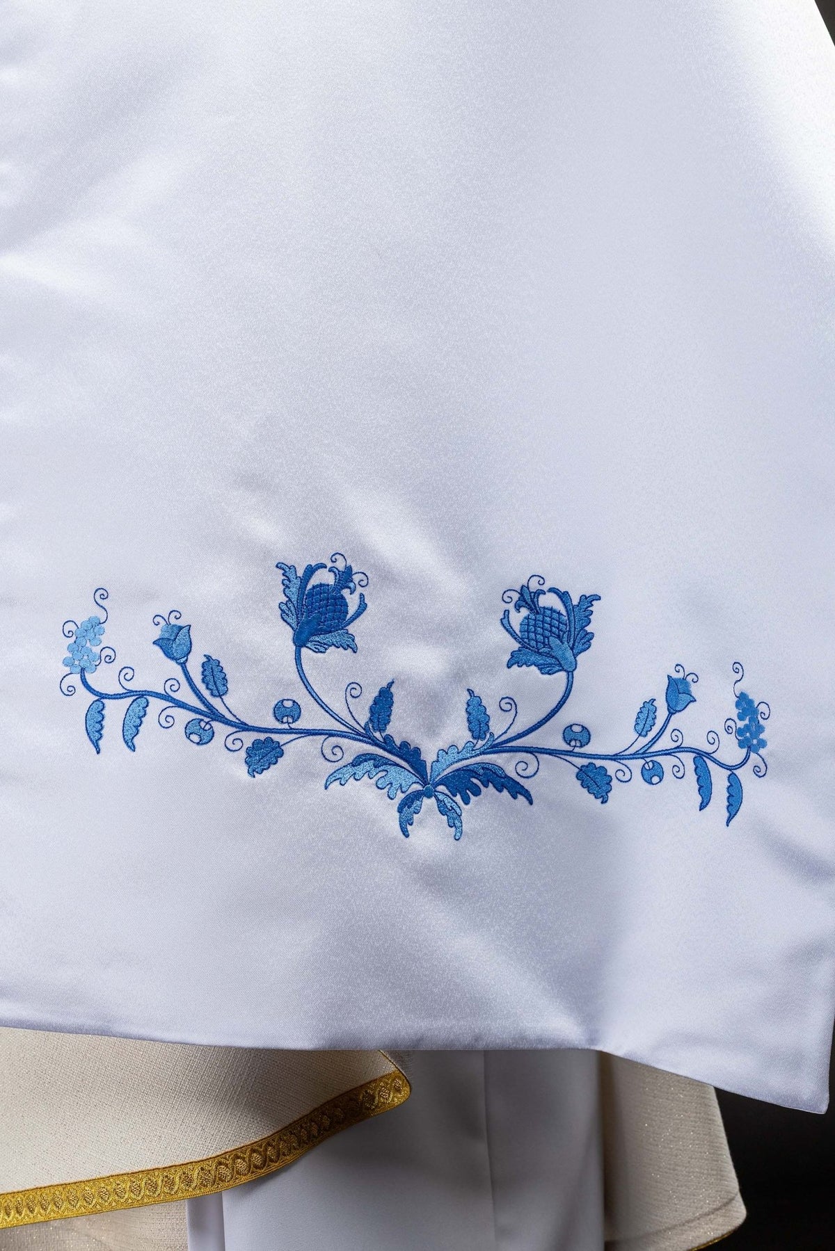 Close-up of the white humeral veil showing blue floral embroidery along the lower edge