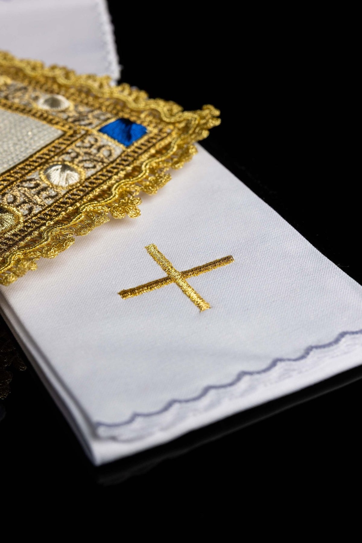 Detail view of the chalice linen set showing a gold embroidered cross and scalloped white edge