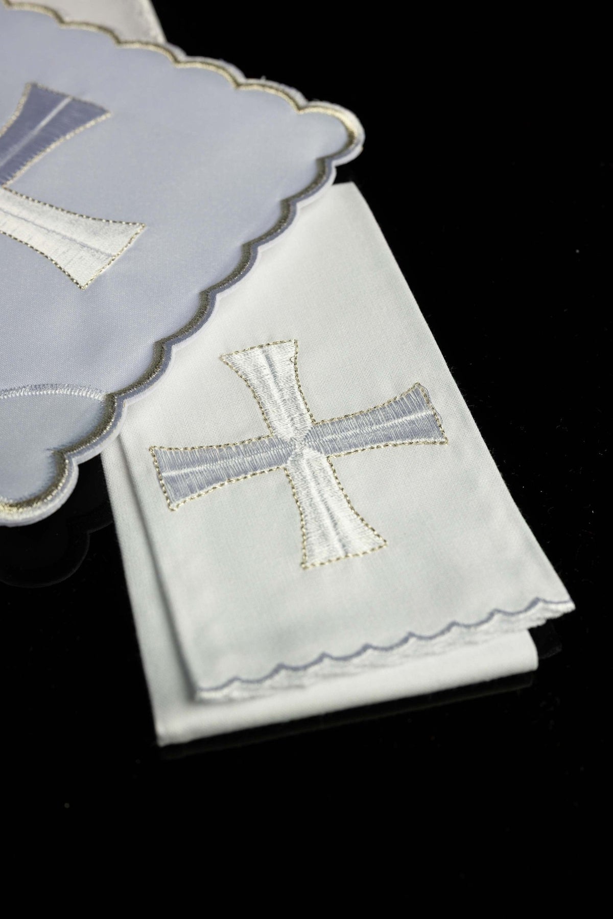 Folded view of chalice linens showing a white embroidered cross and scalloped edges