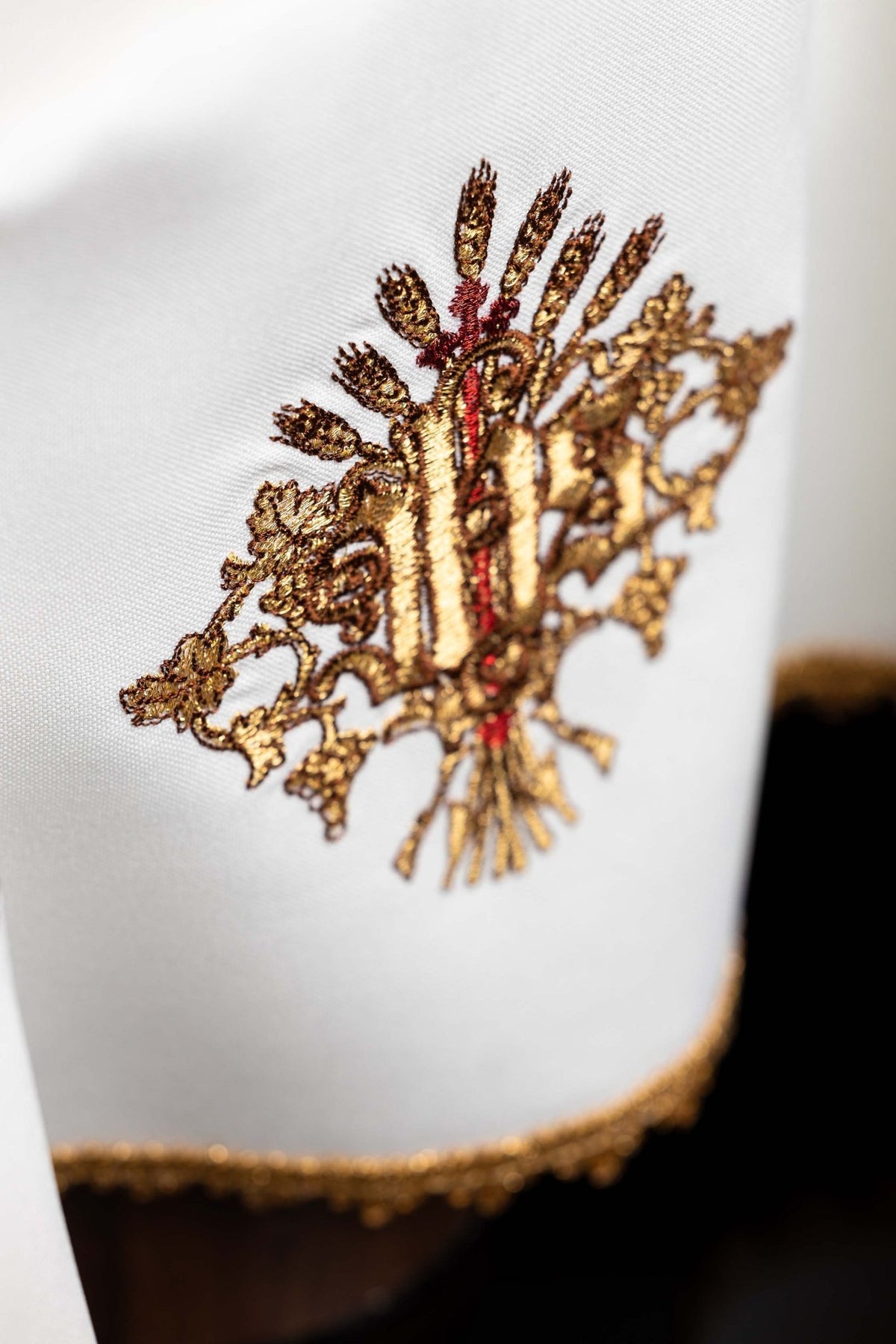 Angled close-up of chalice veil showing raised gold IHS embroidery and gold trim