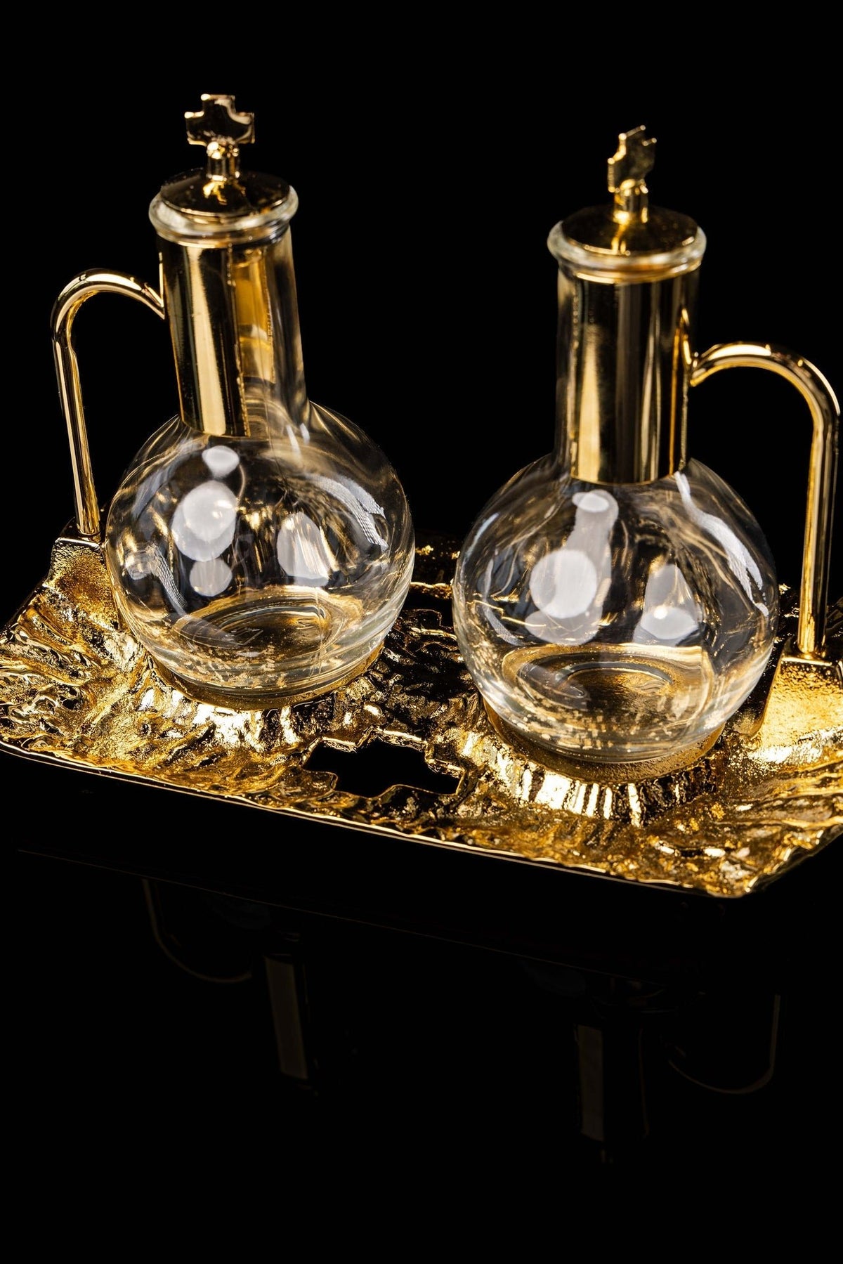 Close-up of paired liturgical cruets with gold-plated necks, handles, and cross-topped lids