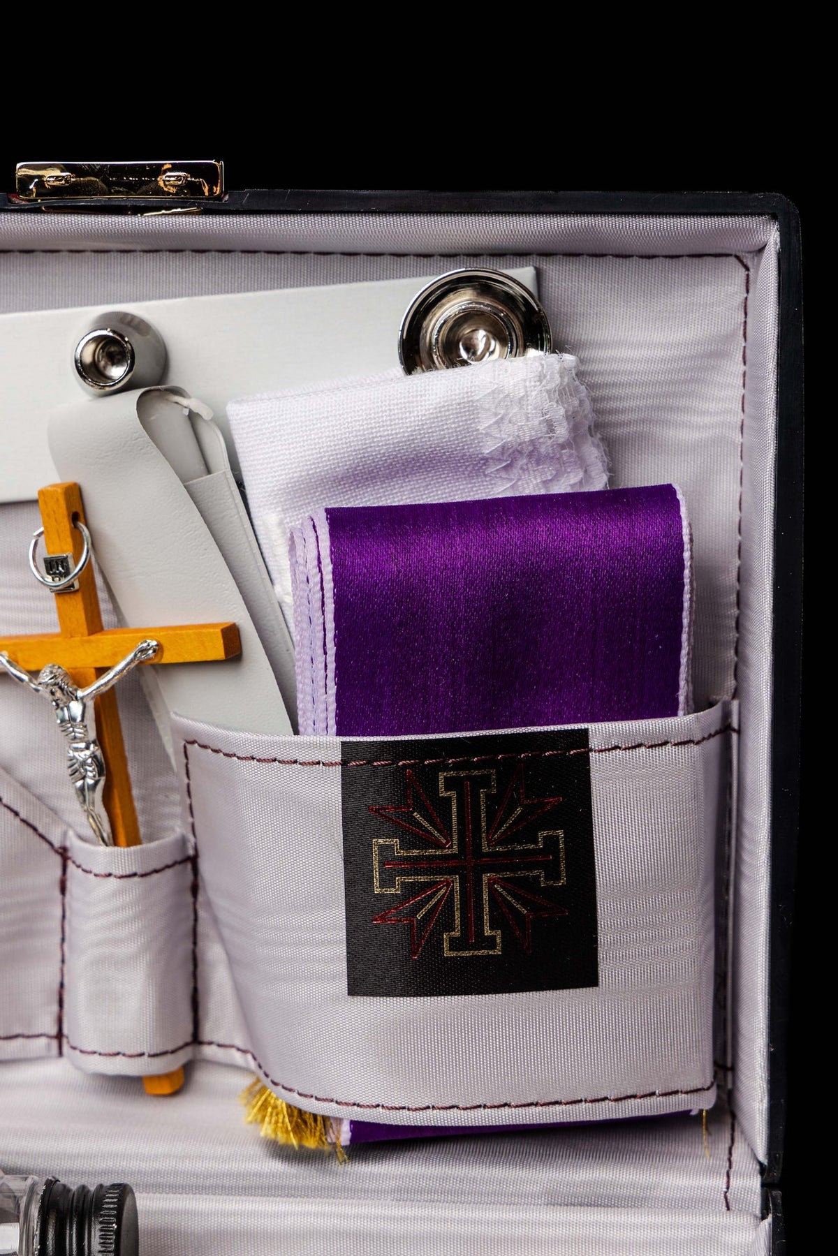 Close-up of equipment suitcase pocket holding folded purple linen with cross emblem