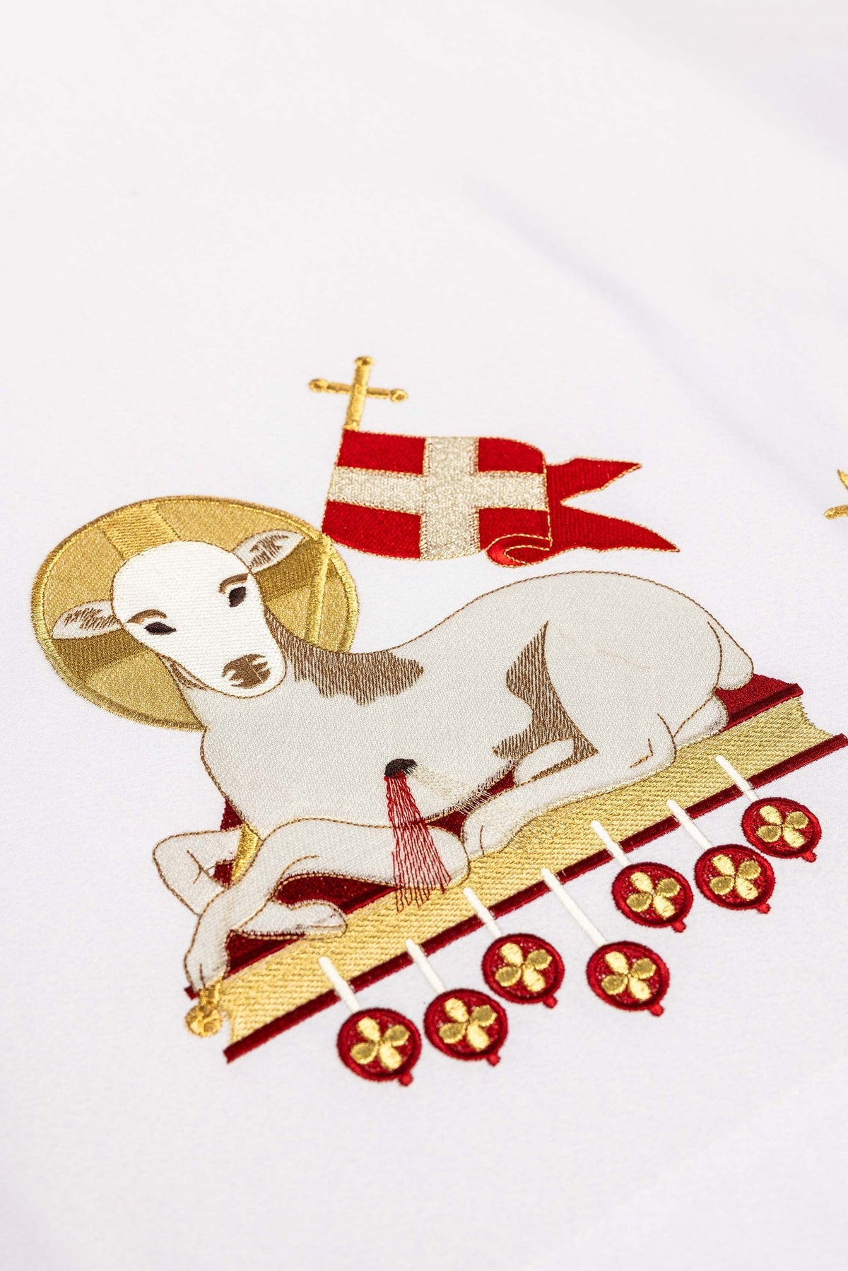 Detail of the Easter altar cloth showing the lamb embroidery, red banner, cross, and hanging red medallions