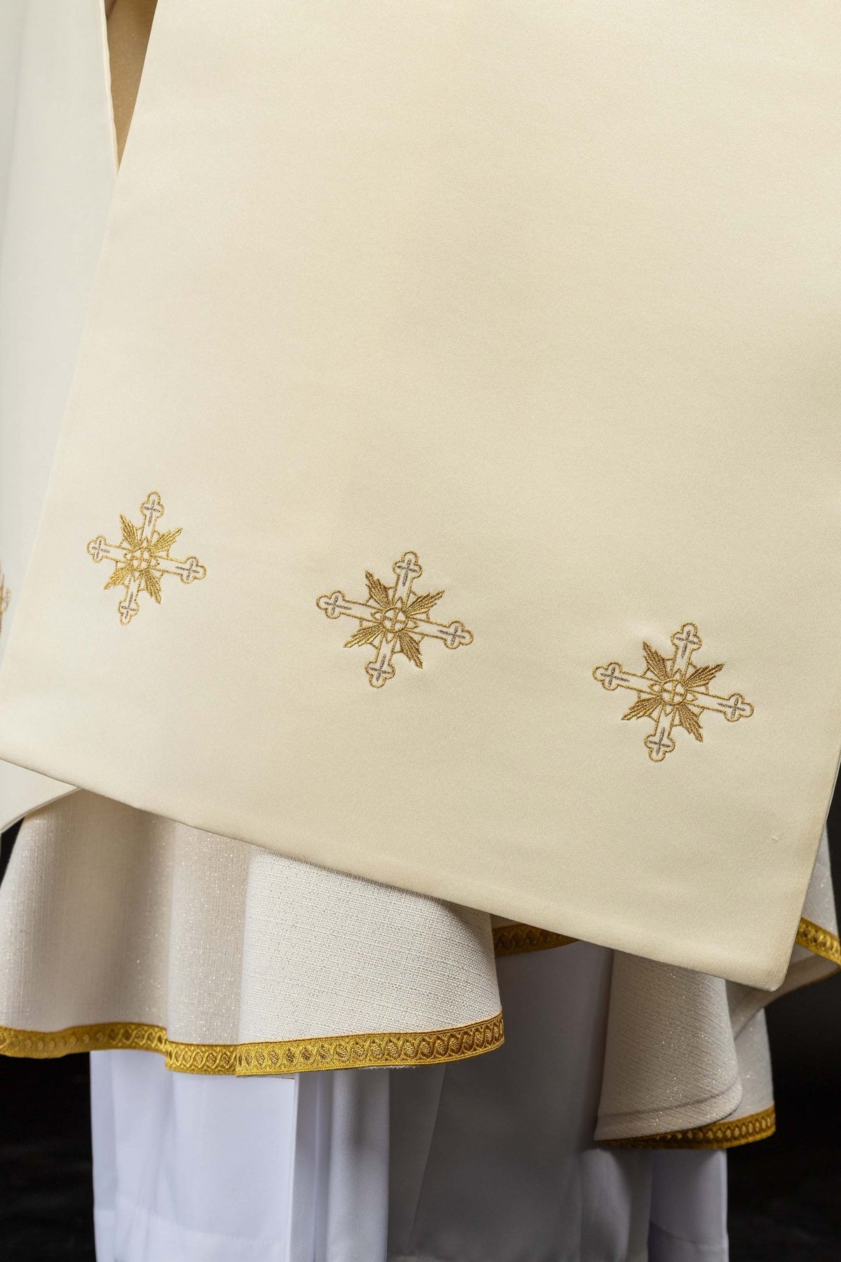 Detail of the ecru humeral veil showing repeated embroidered cross motifs and gold edging