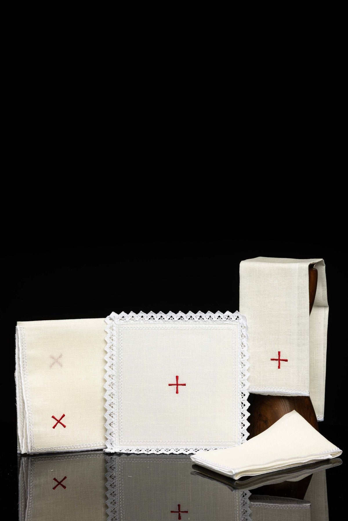 Front view of an embroidered altar linen with a small red cross, cream fabric, and white lace trim