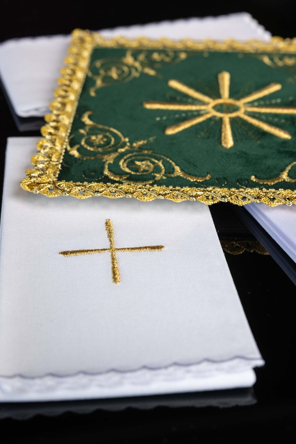Close-up of green velvet chalice linens set with gold trim and white linens bearing embroidered crosses