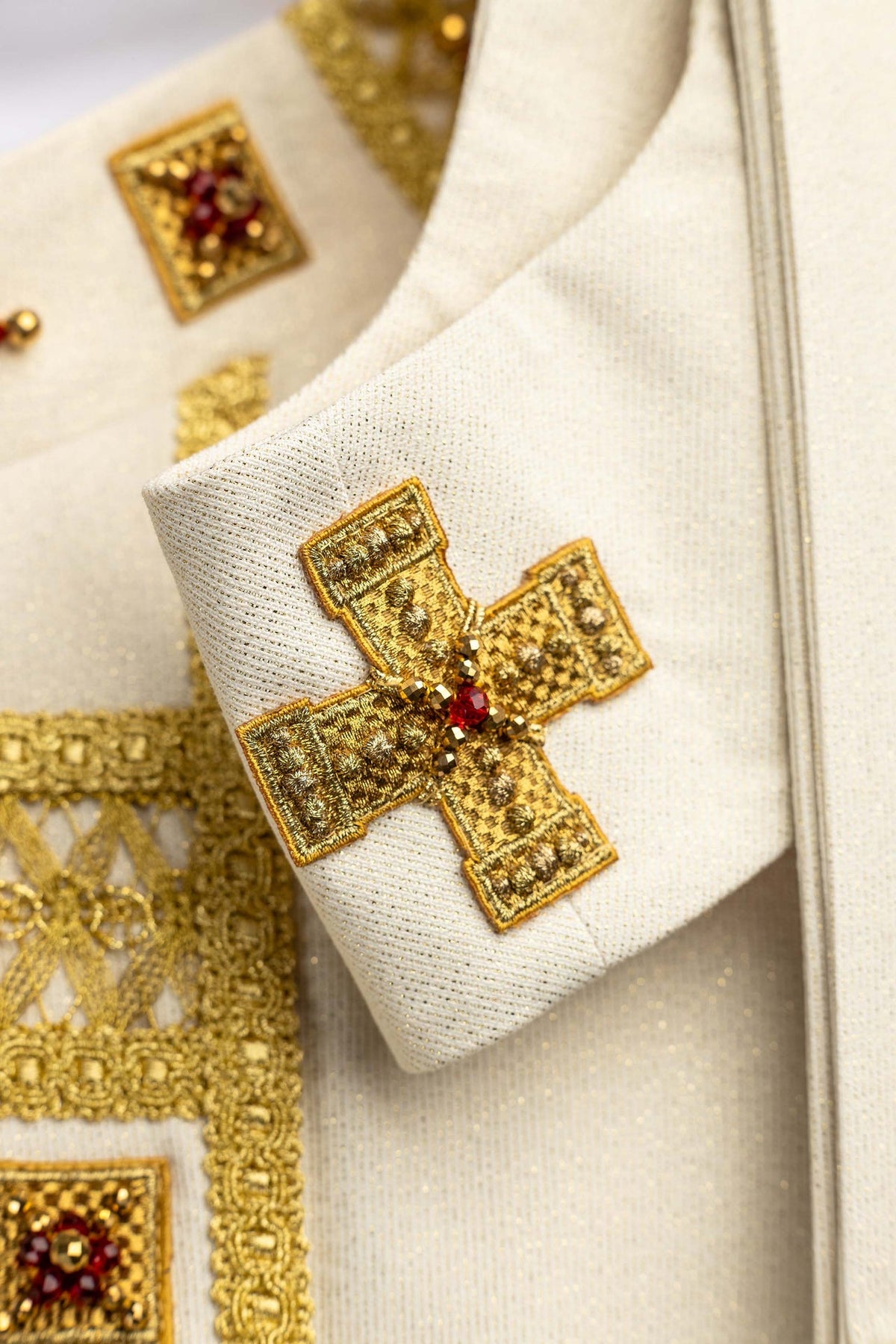 Close-up of a white handmade chasuble with gold cross embroidery and red natural stones