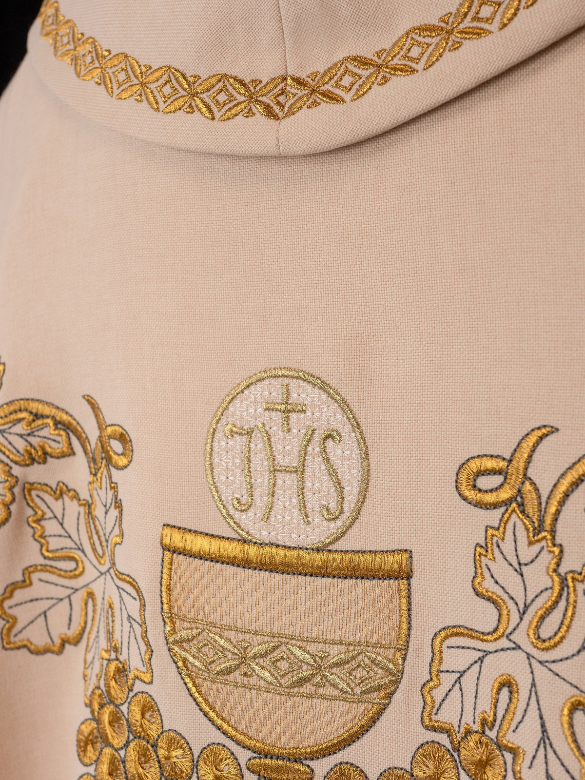 Upper detail of the ecru chasuble showing the IHS emblem, chalice and gold collar trim
