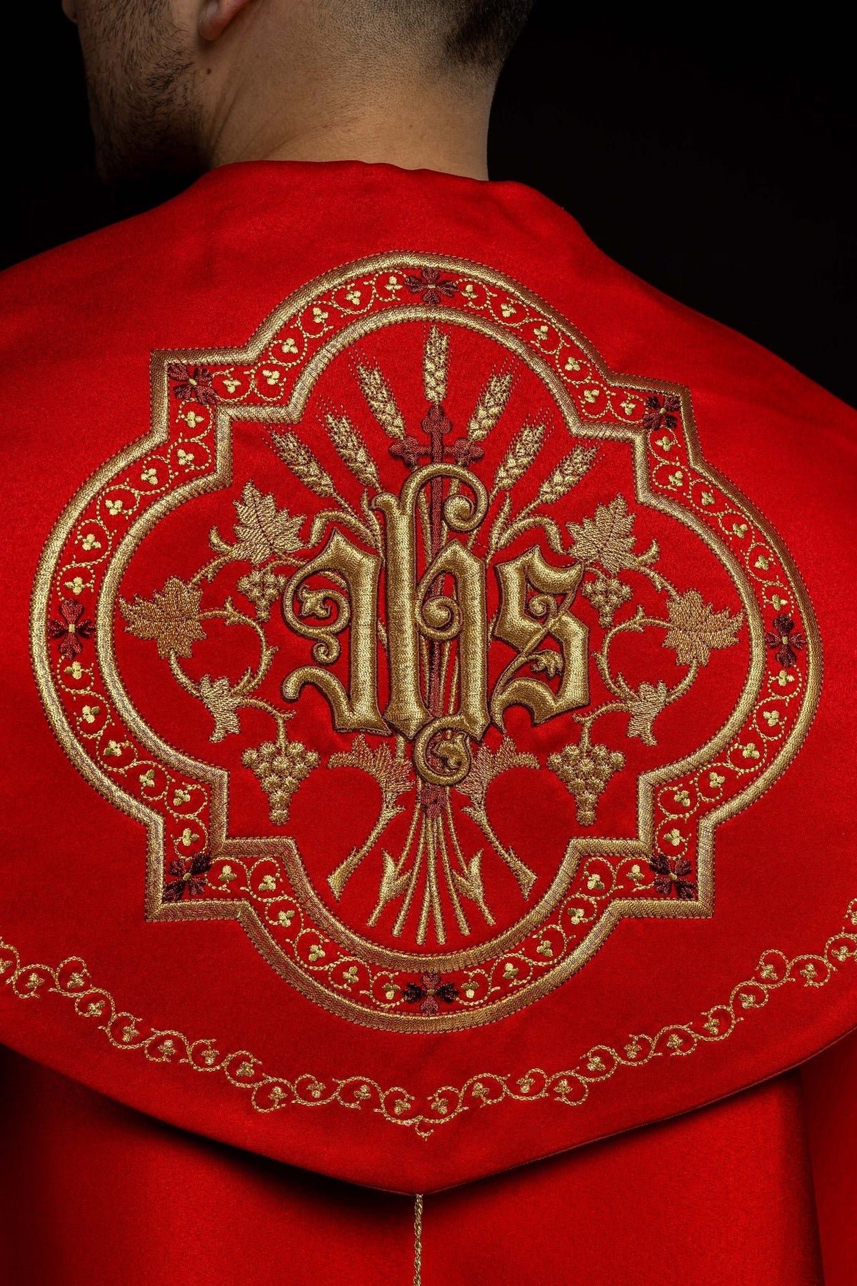 Close-up of red cope back showing ornate gold IHS embroidery and floral border