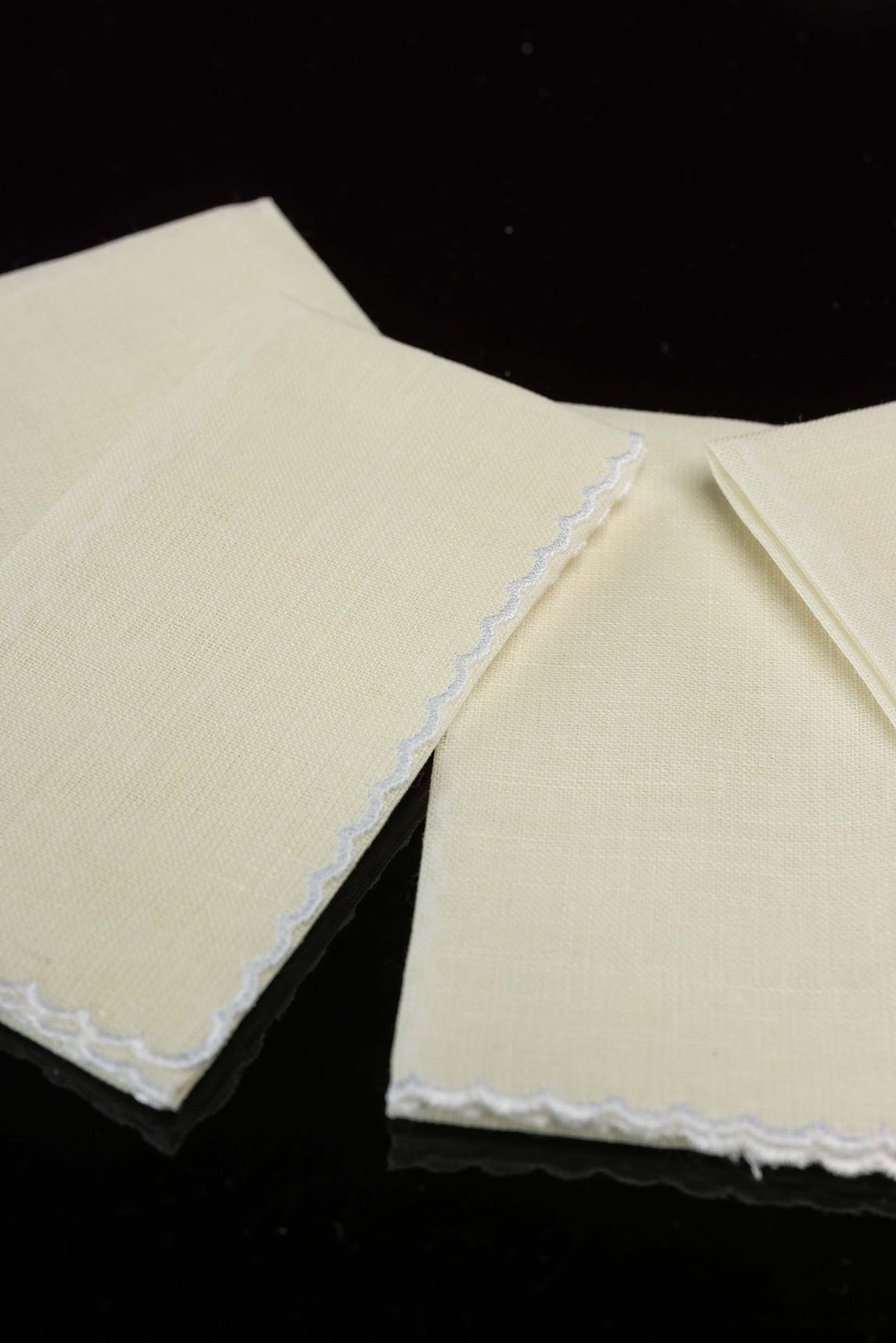 Close-up of the lavabo towel set showing white wavy border embroidery on ecru linen