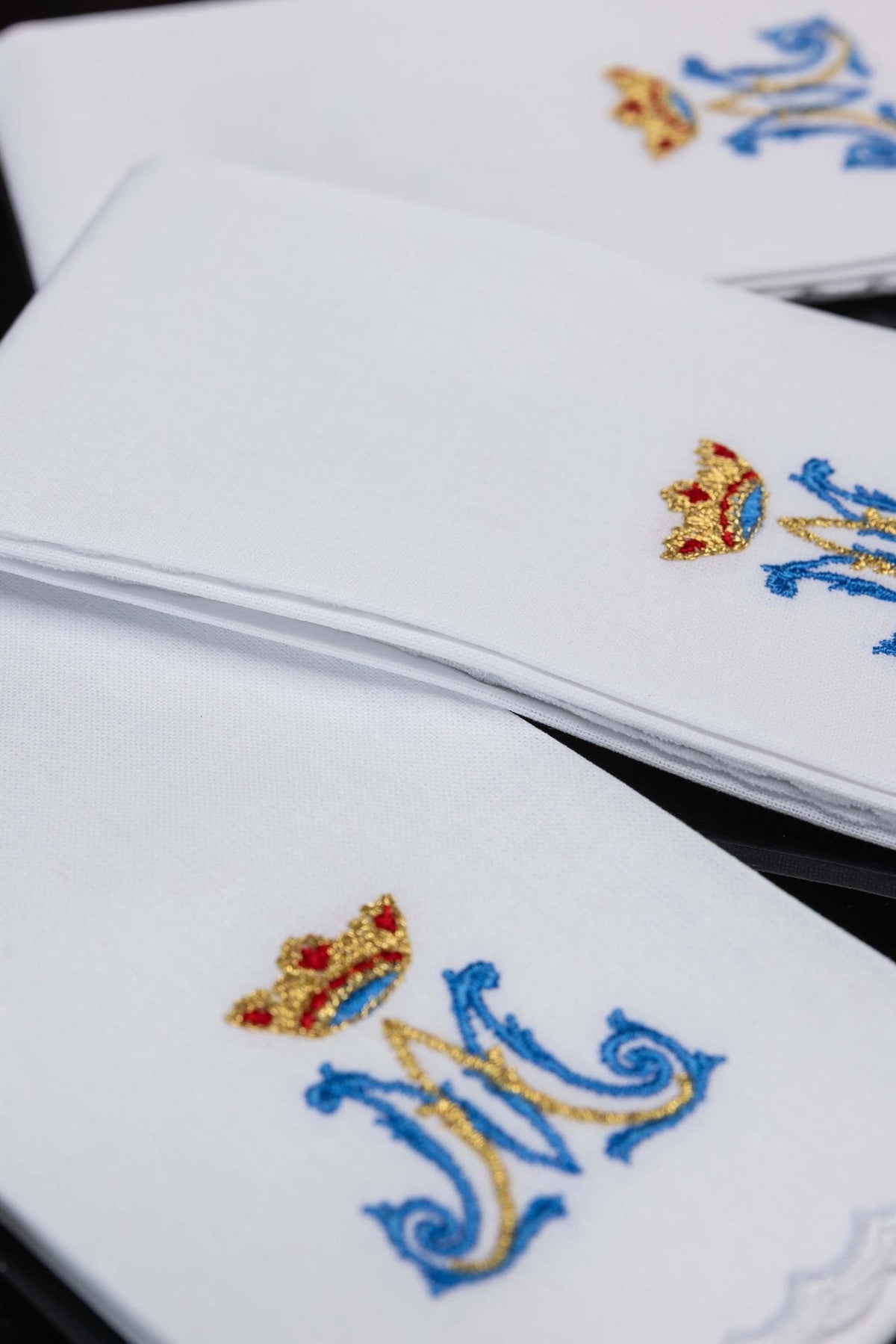 Close-up of white purificators with blue and gold Marian motif embroidery and scalloped edges