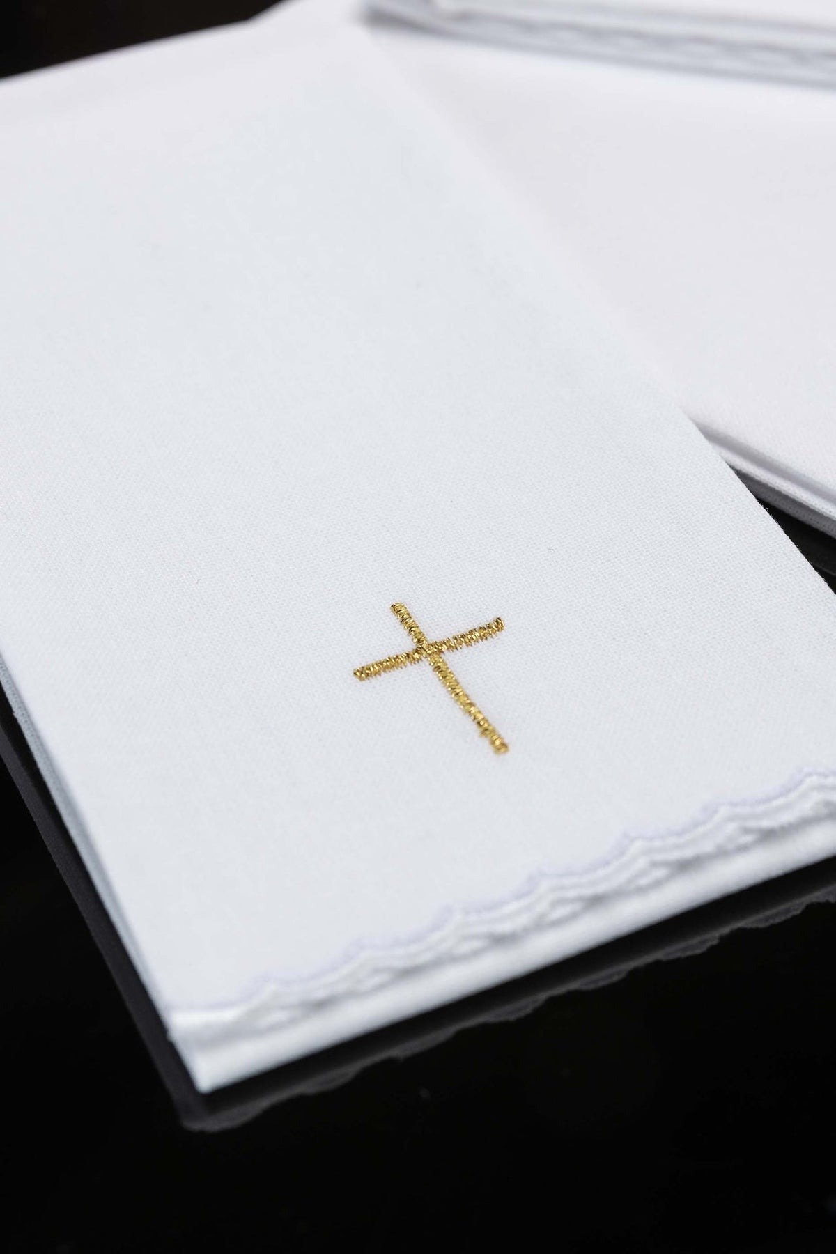 Close-up of white purificators with gold cross embroidery and scalloped edges