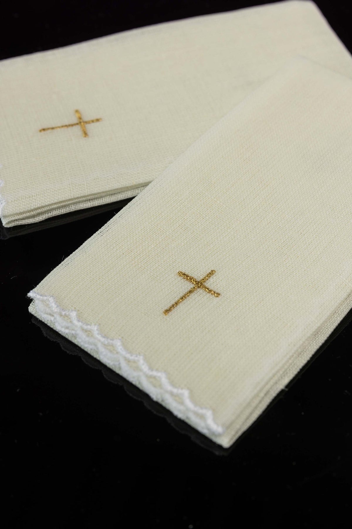 Close-up of purificator set with gold cross embroidery on ecru linen and scalloped white edging