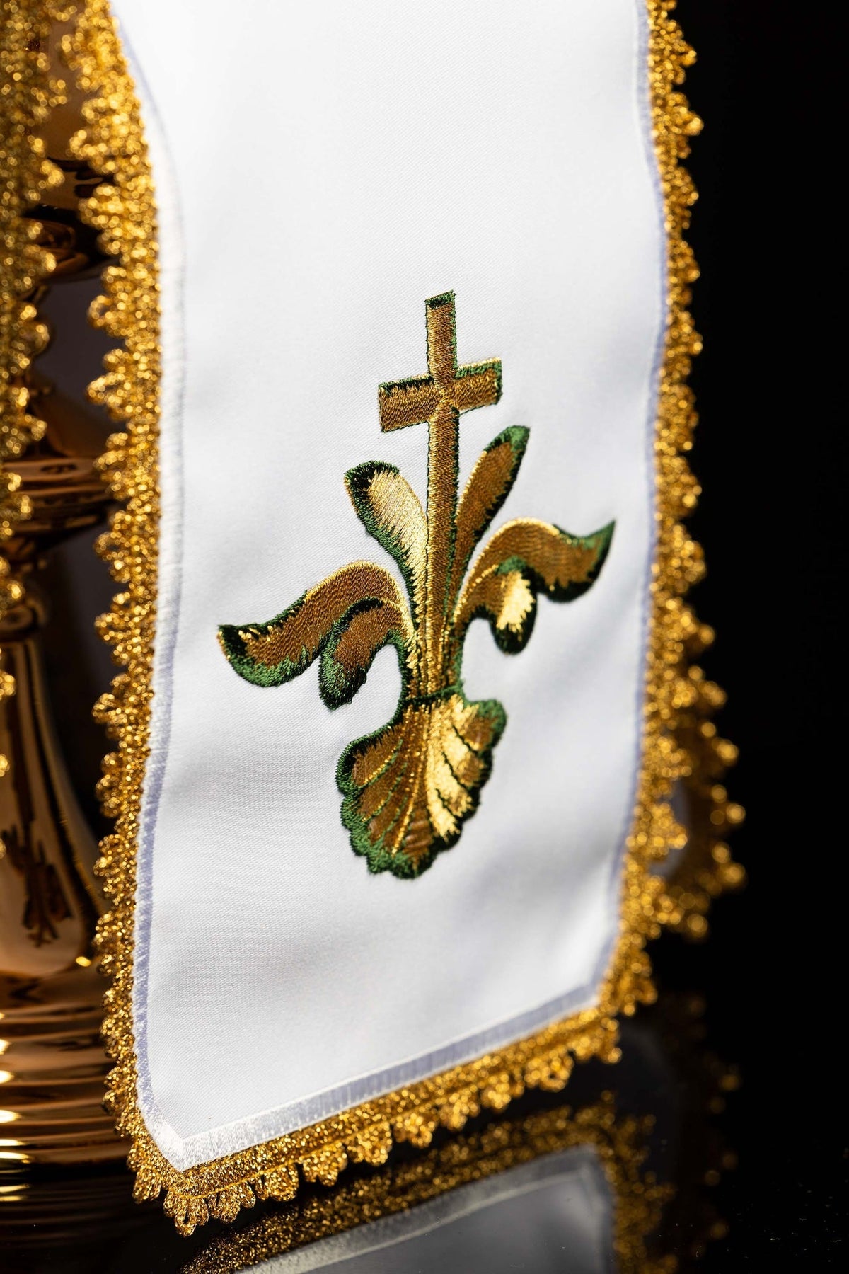 Close-up of the white ciborium veil showing a green-gold embroidered cross and floral motif