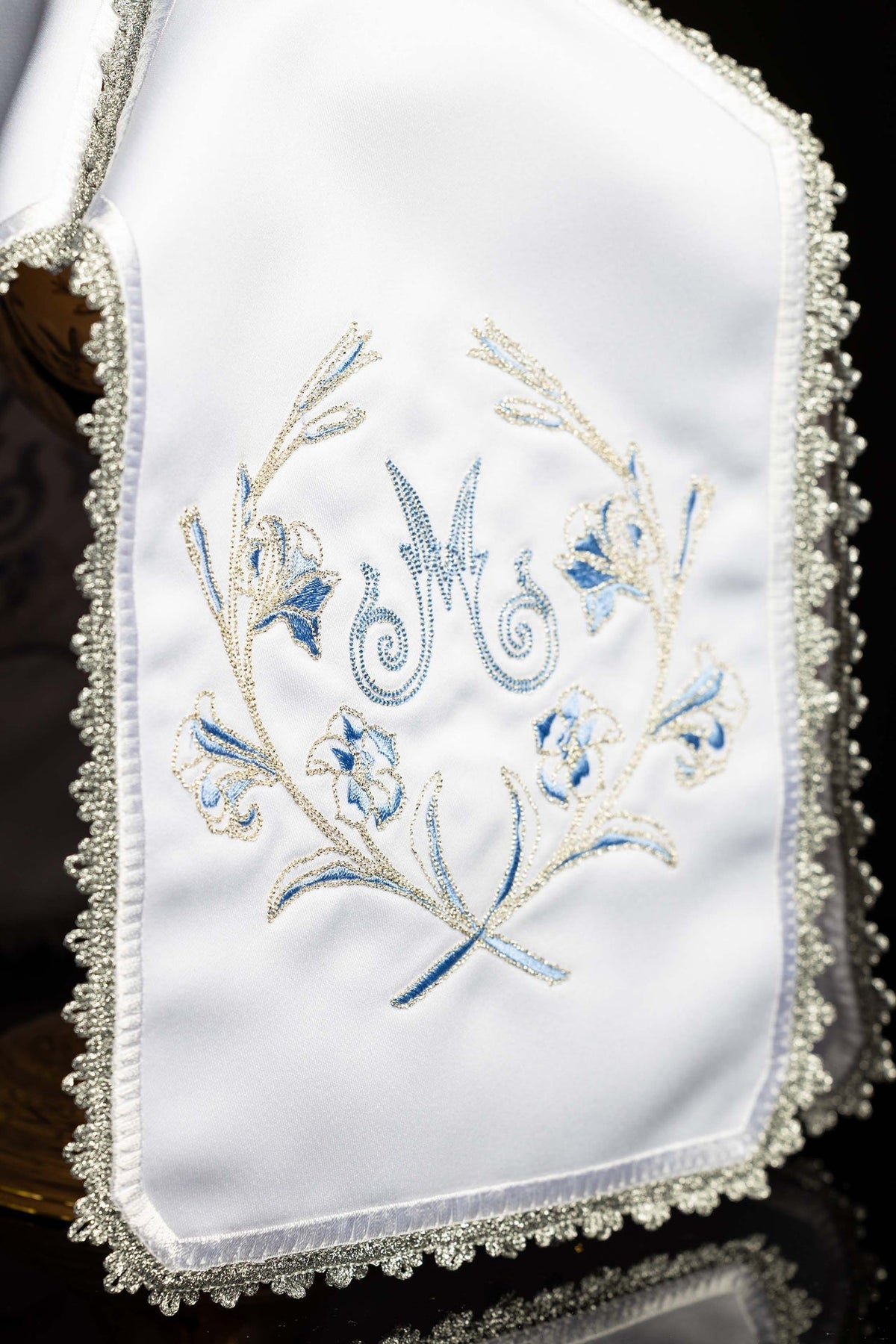 Close-up of ciborium veil showing blue Marian monogram and floral embroidery on white fabric
