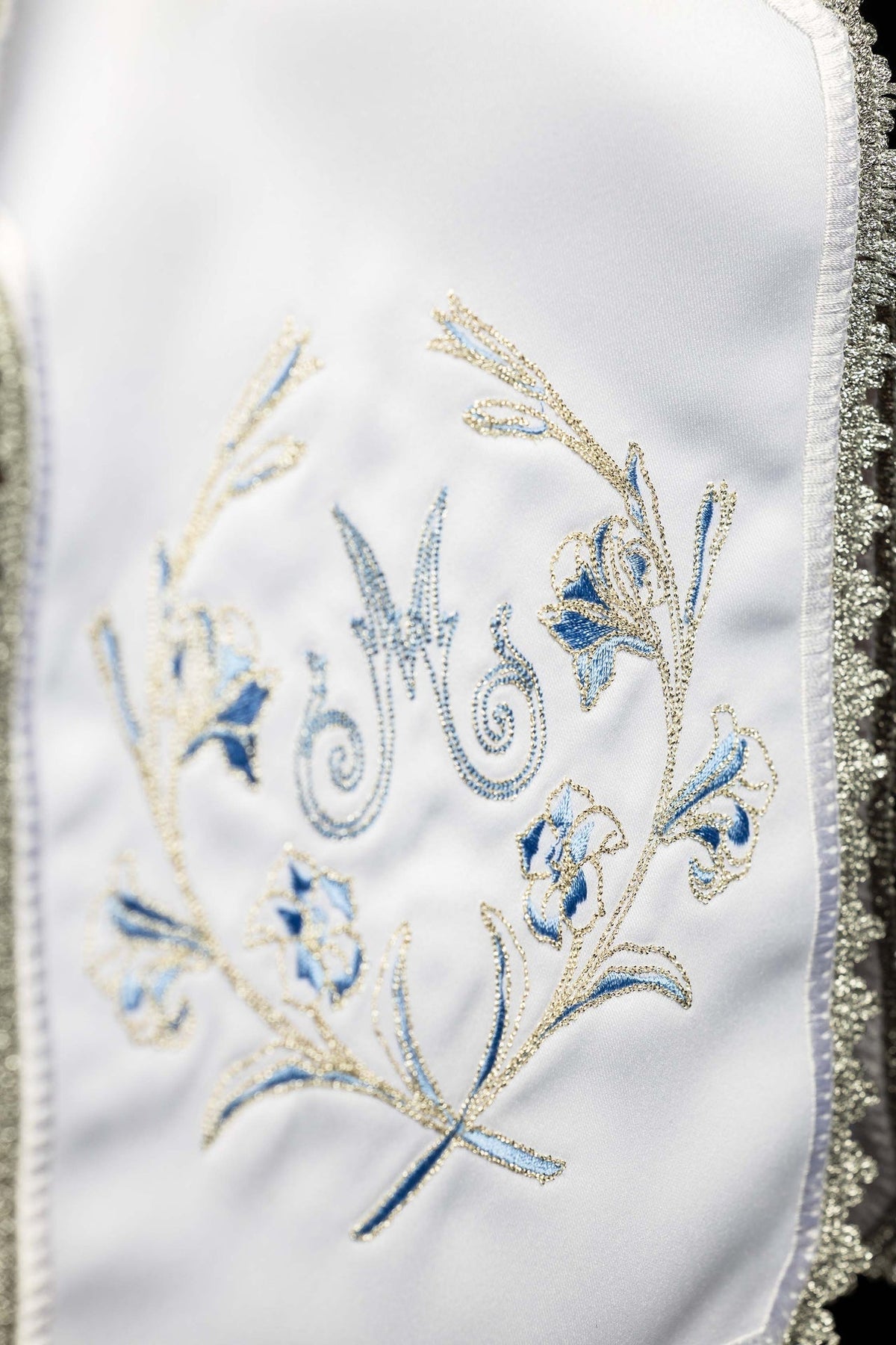 Detail view of ciborium veil showing blue and gold Marian monogram with floral embroidery