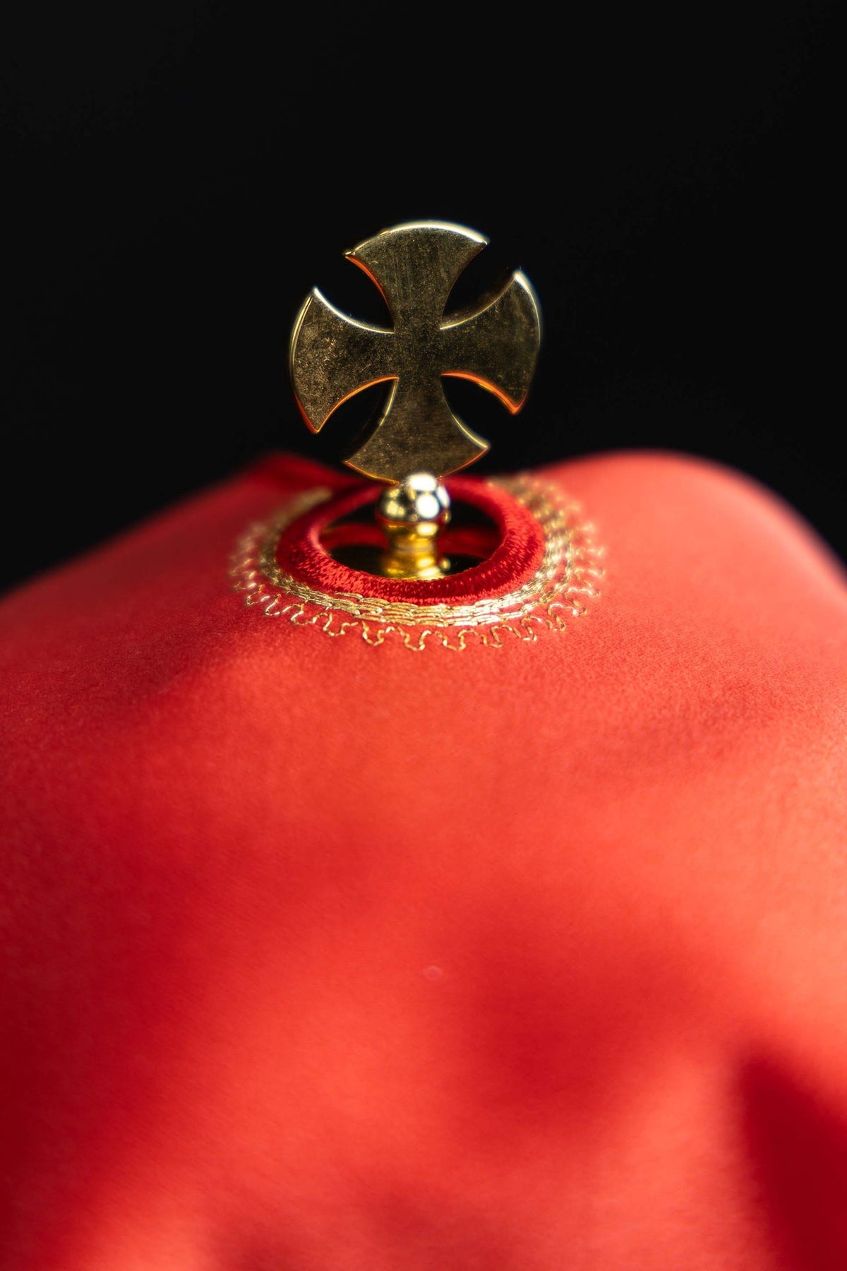 Top detail of a red ciborium veil with a metal cross finial and gold trim