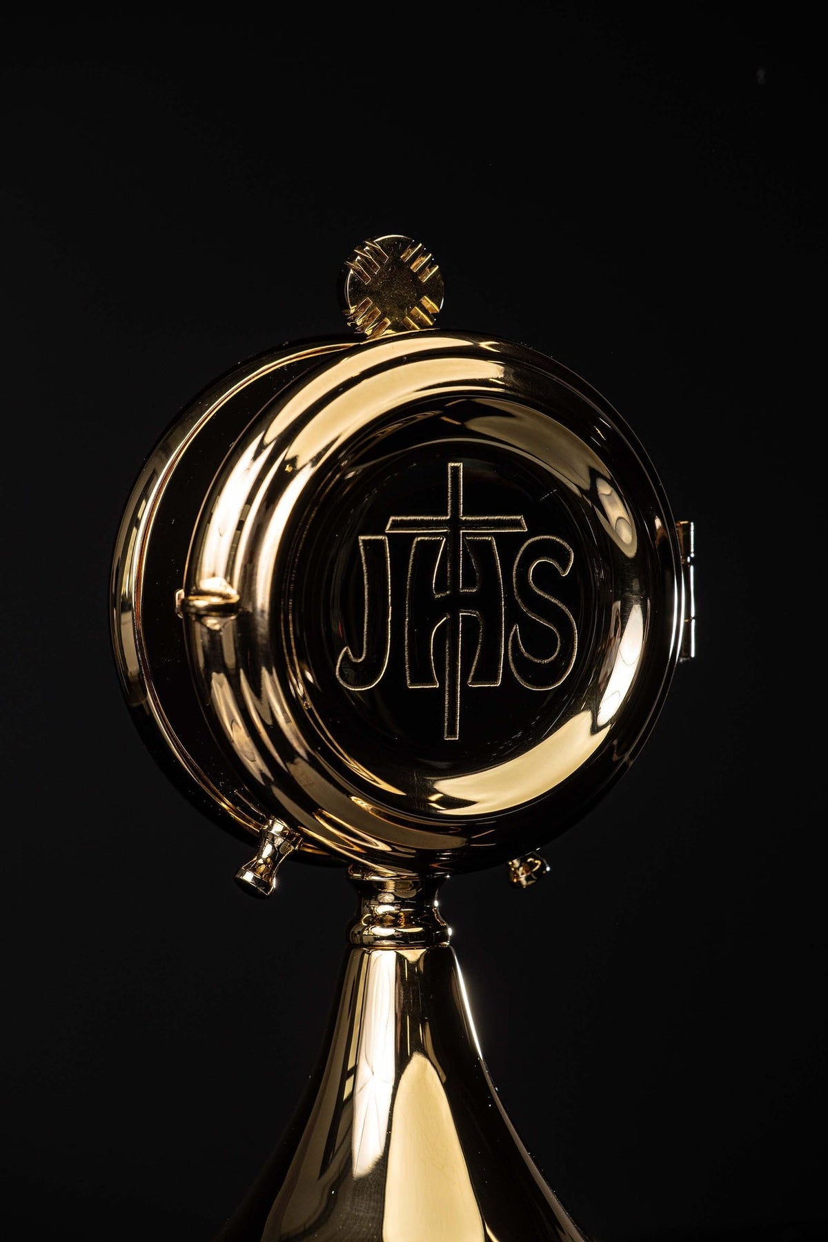 Close-up front view of the brass custodia showing the IHS emblem and cross finial