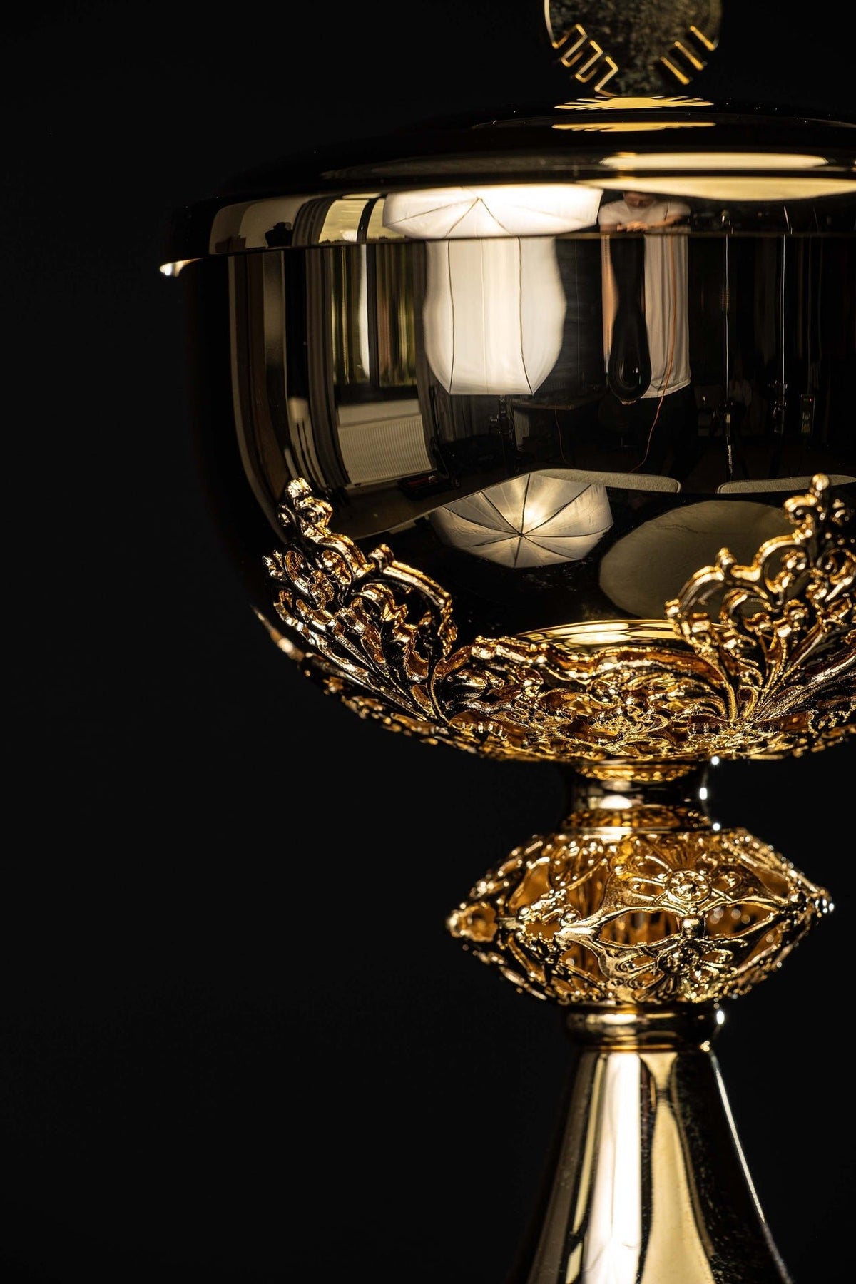 Angled view of gilded brass ciborium showing floral relief around the bowl and decorated base