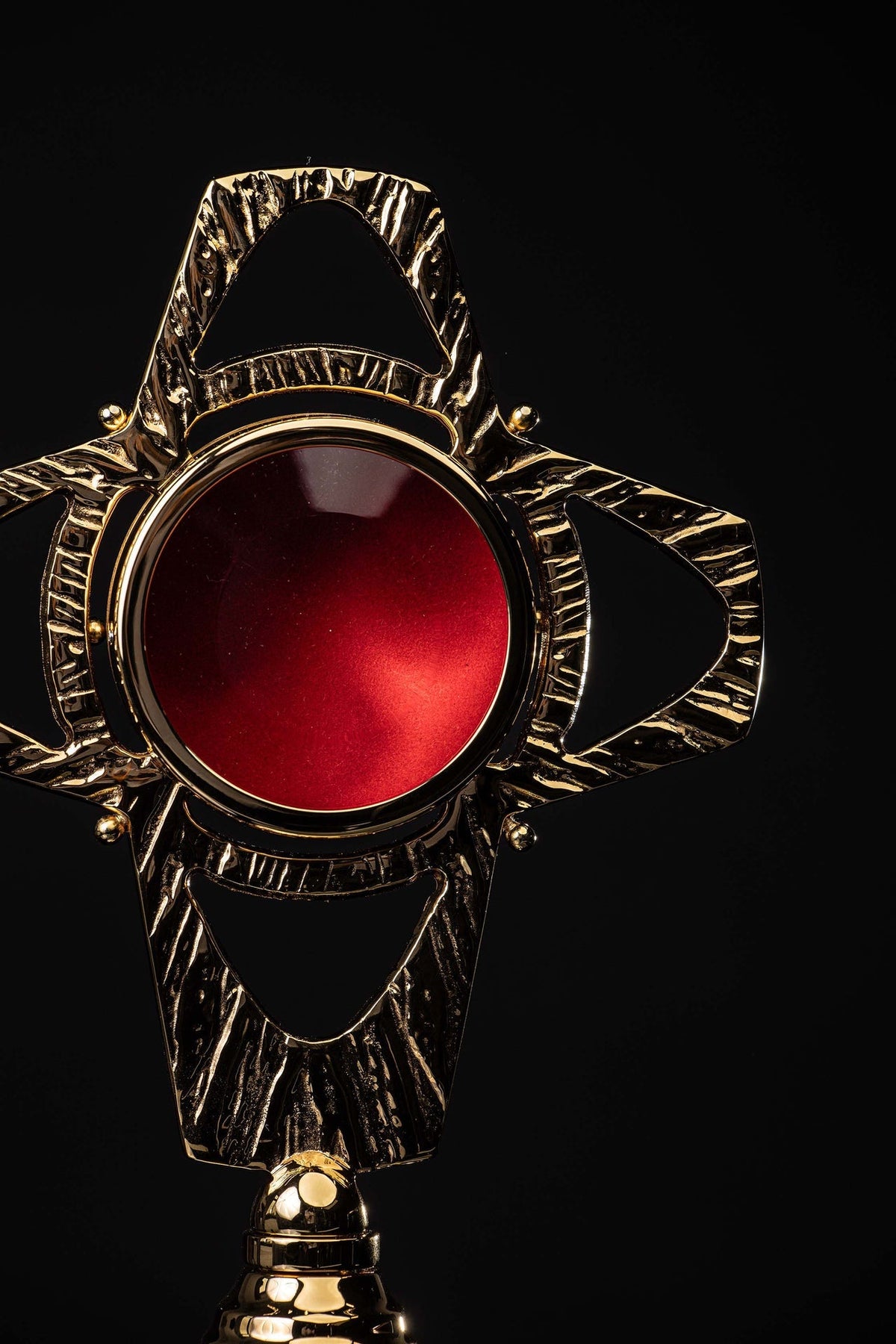 Close-up front view of the cross-shaped reliquary showing its red center and radiating textured brass details
