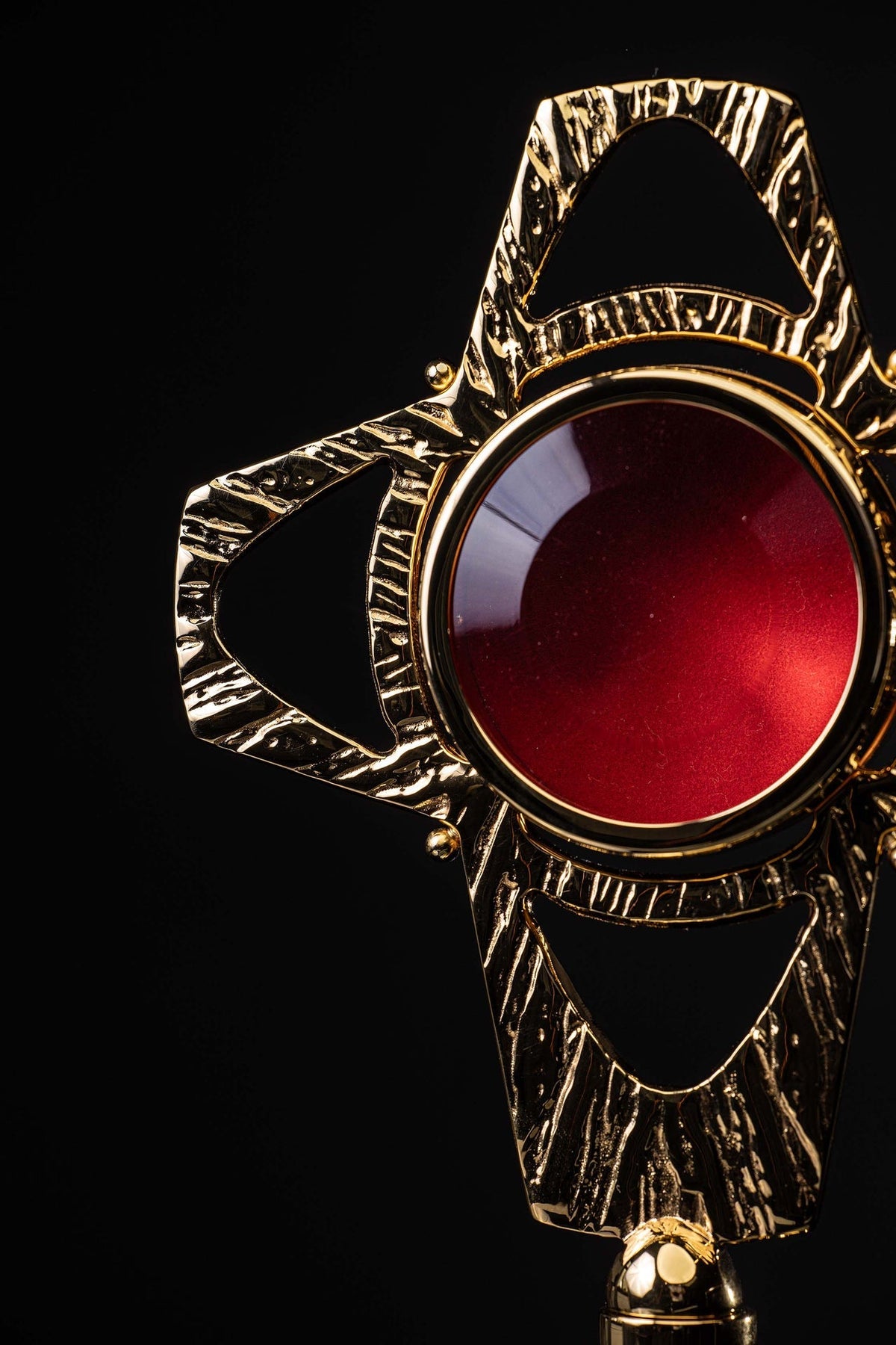 Angled close-up of the cross-shaped reliquary showing the red center, gilded rim and textured arm