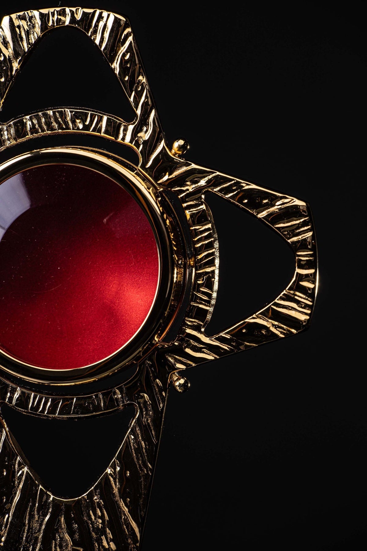 Close-up of the reliquary's gilded brass cross arm, red center and raised textured detailing